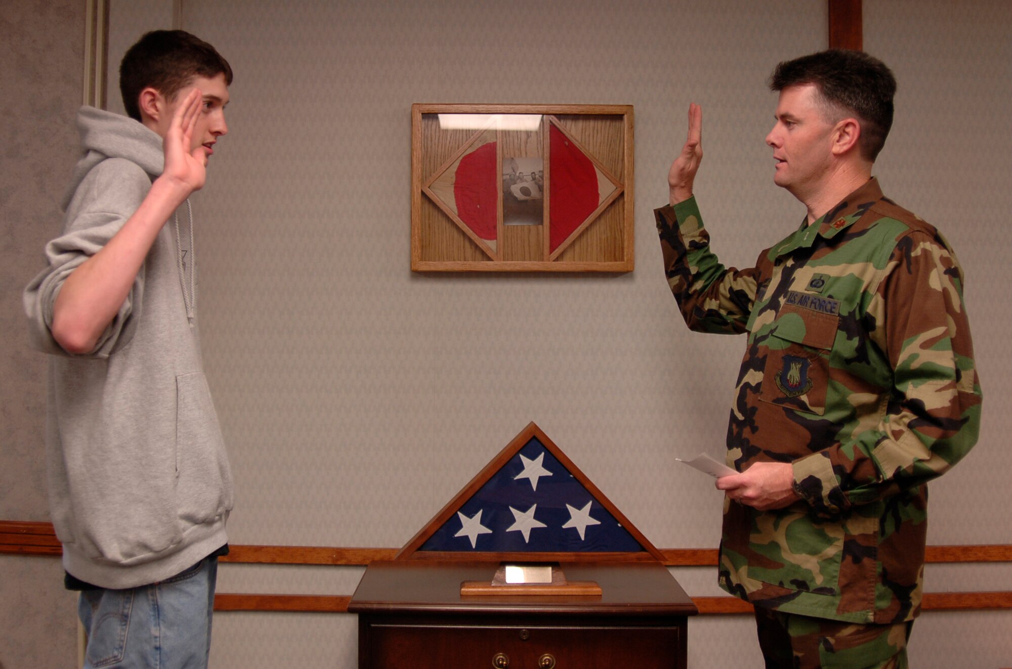 MCCONNELL AIR FORCE BASE, Kan. -- Maj. Mark Snow, 22nd Comptroller Squadron commander, administers the Oath of Enlistment to his son Elliot Snow, Dec. 21. The ceremony was held in Maj. Snow’s office in front of his grandfather’s casket flag and World War II photo which includes two captured Japanese flags. (Photo by Airman 1st Class Maria Ruiz)