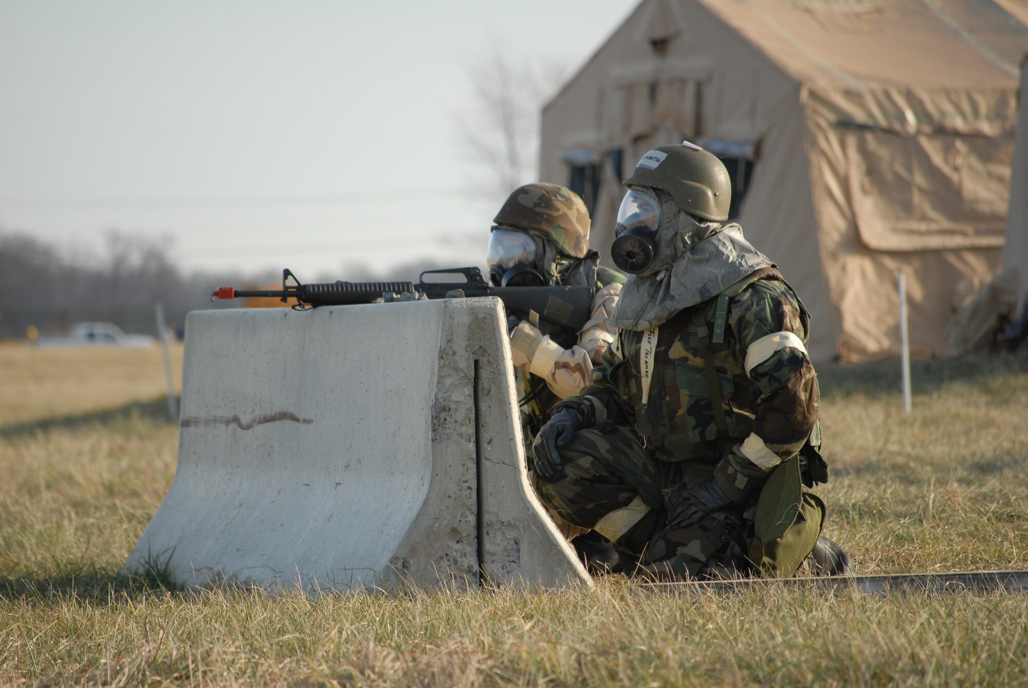 Tech. Sgt. Jesse Talamantes, 9th Airlift Squadron, and Staff Sgt. Andrew Gassner, 9th AS, seek protection behind a concrete barrier and protect their tent during Dover Air Force Base's Haunted House Battle Axe exercise Jan. 7. Defensive measures was one of the many skills practiced during the exercise. (U.S. Air Force photo/Tech. Sgt. Kevin Wallace)