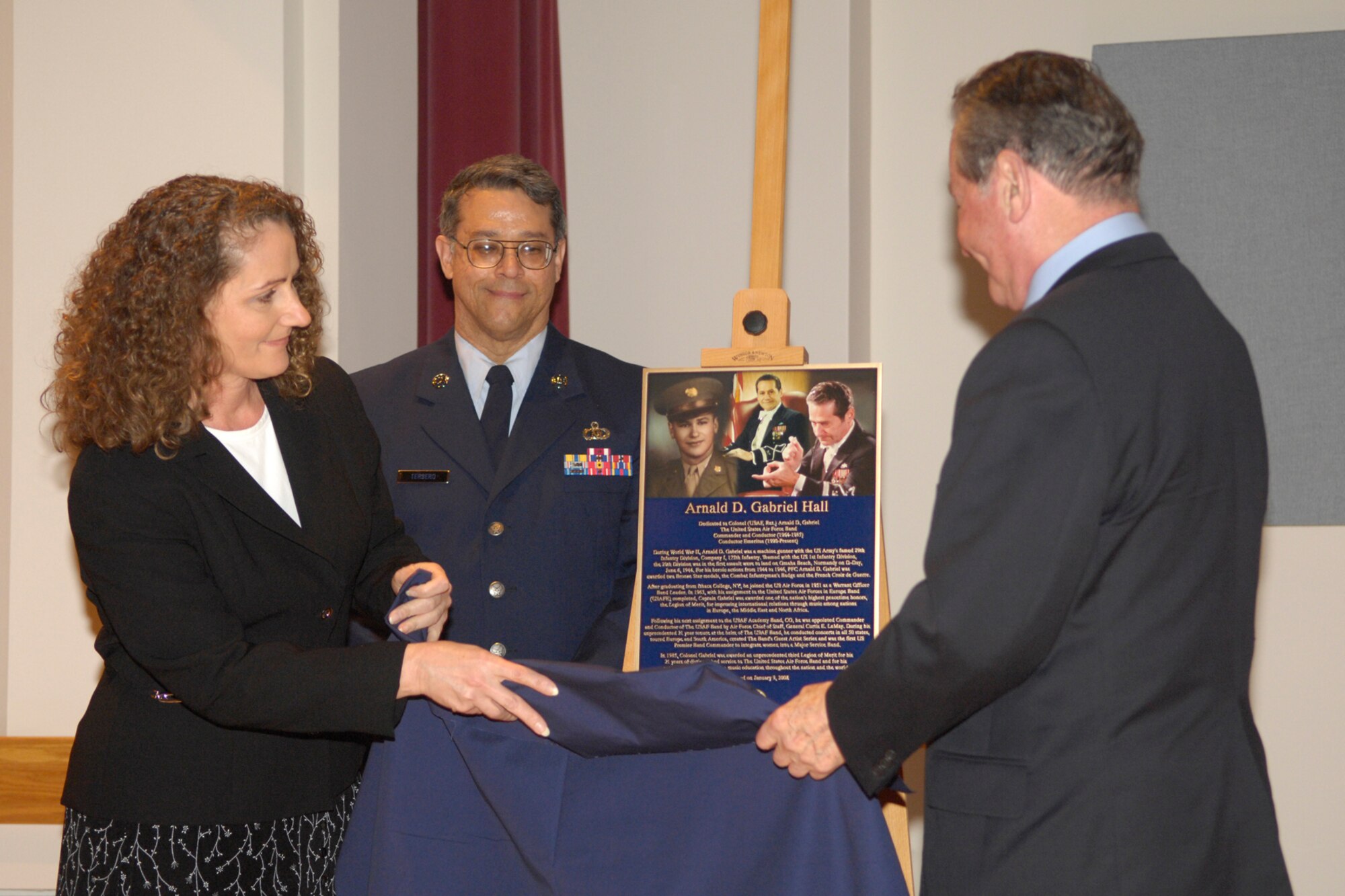 As Joanne Murphy, his daughter, and Chief Master Sgt. Joe Tersero look on, retired Col. Arnald D. Gabriel, conductor emeritus and former commander of The Band, gets his first glimpse at the plaque renaming the “virtual room” at The Band’s headquarters in his honor. (U.S. Air Force photo by Airman 1st Class Sean Adams.)
