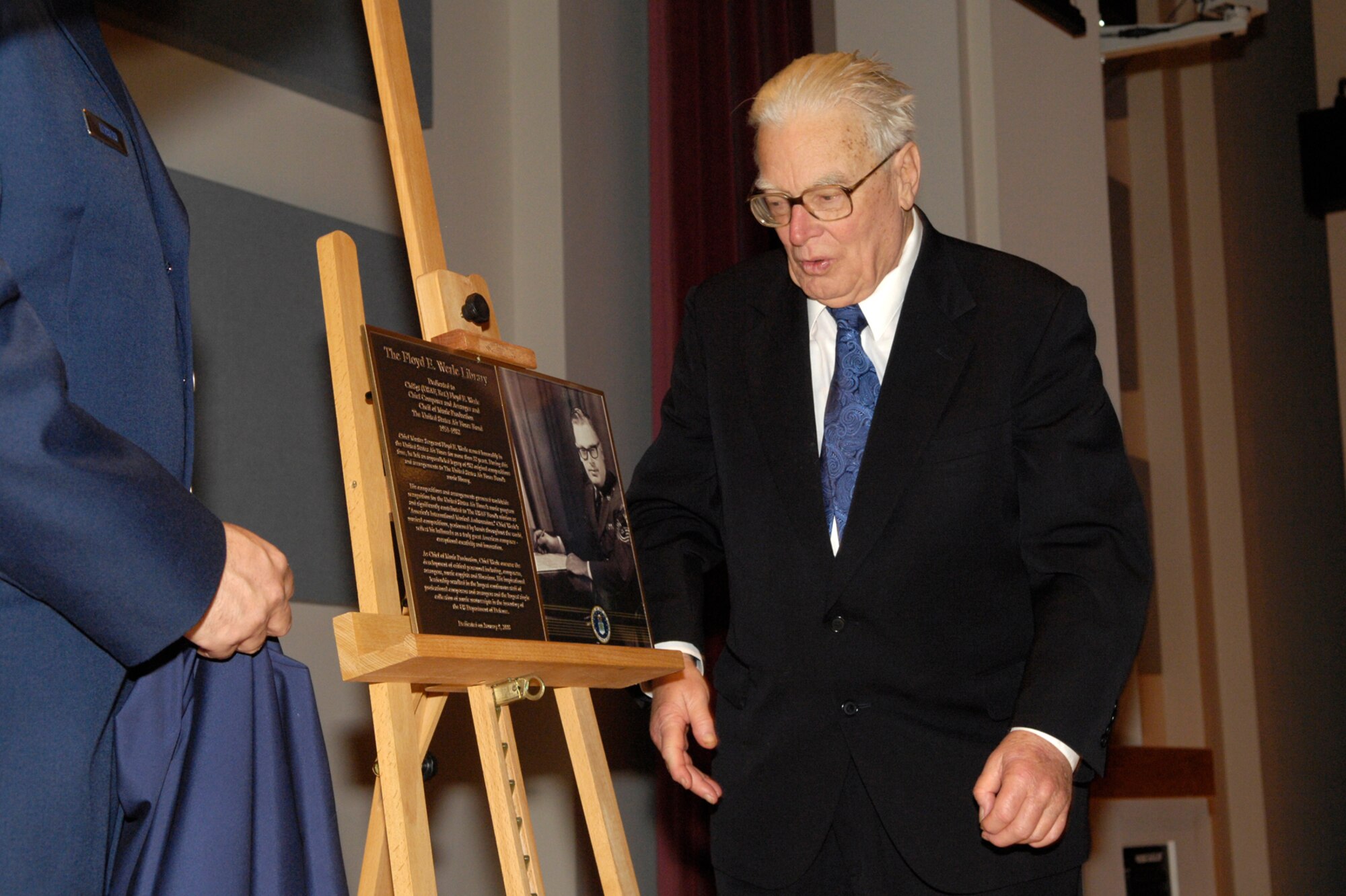 Retired Chief Master Sgt. Floyd Werle, composer and arranger emeritus of the U.S. Air Force Band, looks on as the plaque dedicating the Werle Library is unveiled Jan. 9 at Hangar 2. (U.S. Air Force photo by Airman 1st Class Sean Adams.) 