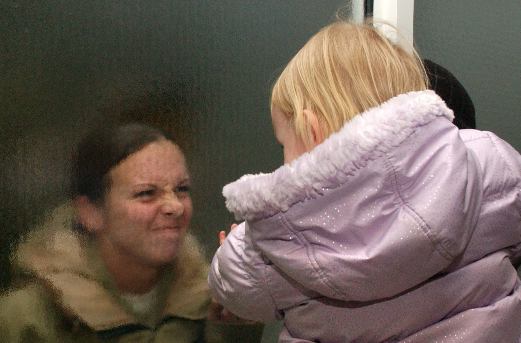 Happy to be home, Staff Sgt. Christy Coshenet, 100th Logistics Readiness Squadron, greets her daughter with a funny face through the frosted glass of the RAF Mildenhall passenger terminal Jan. 11, after returning from a 6-month deployment to Southwest Asia. (U.S. Air Force photo by Staff Sgt. Tyrona Pearsall)