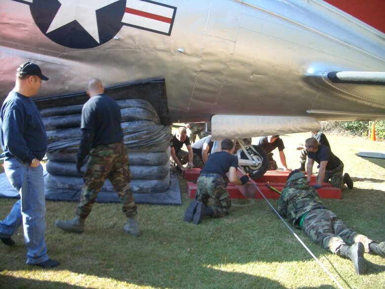 Members of the 43rd Maintenance Squadron look on as Airmen 1st Class Zach Kline and William Howell install wooden beams to keep the aft landing gear of the C-46 Commando in the air Nov. 17, 2007. 