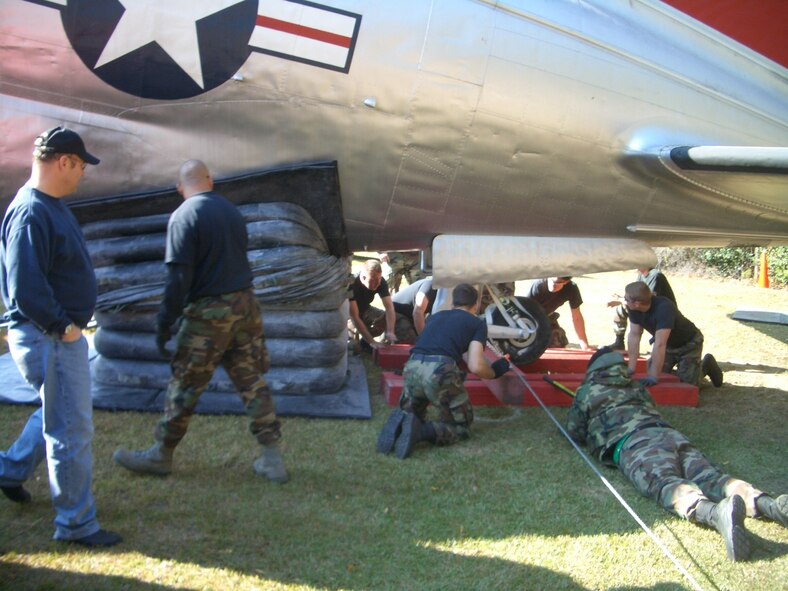Members of the 43rd Maintenance Squadron look on as Airmen 1st Class Zach Kline and William Howell install wooden beams to keep the aft landing gear of the C-46 Commando in the air Nov. 17, 2007. 