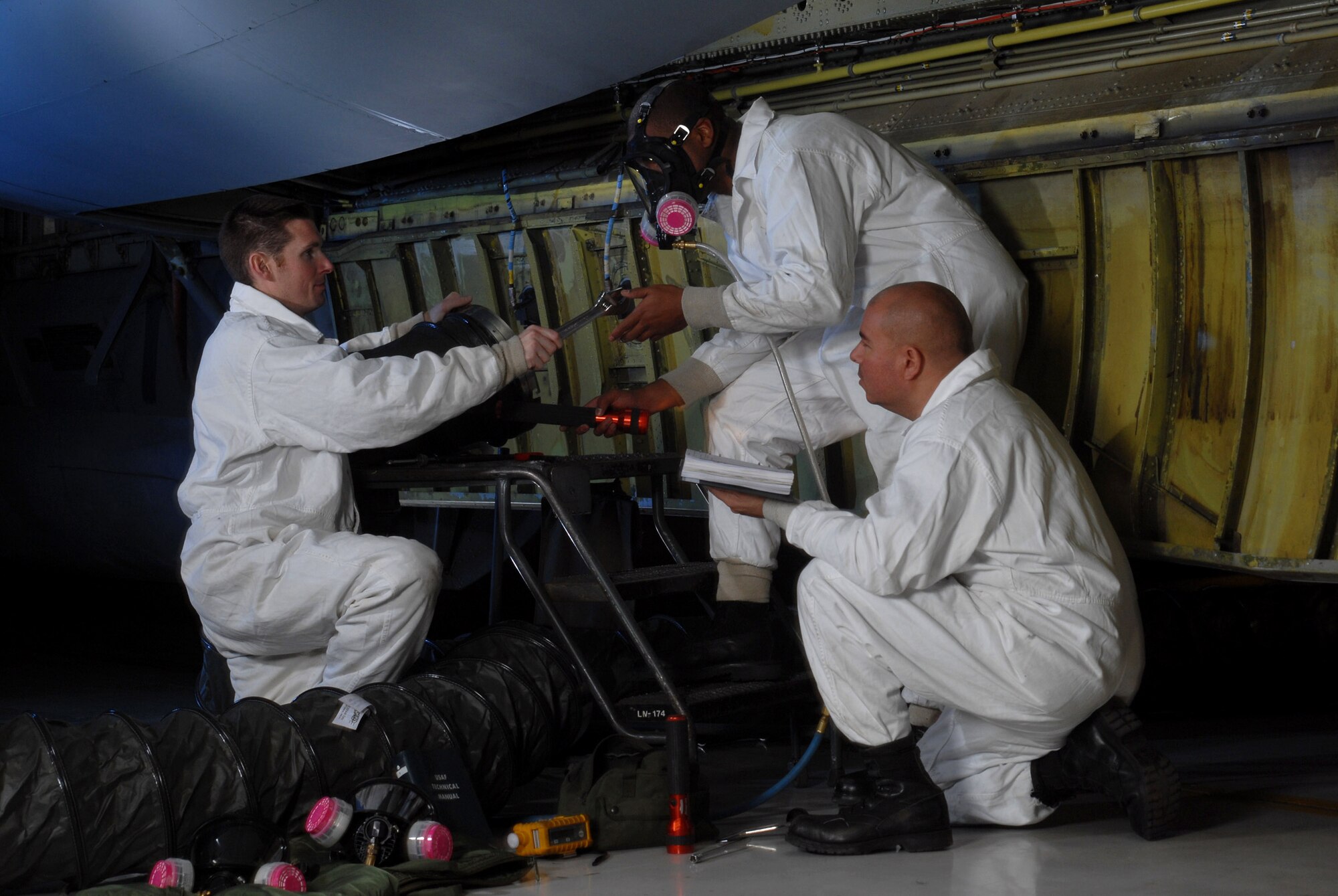 Senior Airman David Skannal, wearing a full-face supplied air respirator (center), receives a wrench from Staff Sgt. Ryan Slanina (left) while Tech. Sgt. Tim Burrola looks on before inspecting the interior of the center wing fuel tank of a KC-135 Stratotanker Jan. 9 at March Air Reserve Base, Calif. Airman Skanalla is wearing the respirator so he could breathe properly while troubleshooting inside the fuel tank for leaks. All three are fuel cell technicians from the 452nd Maintenance Squadron. (U.S. Air Force photo/Val Gempis)