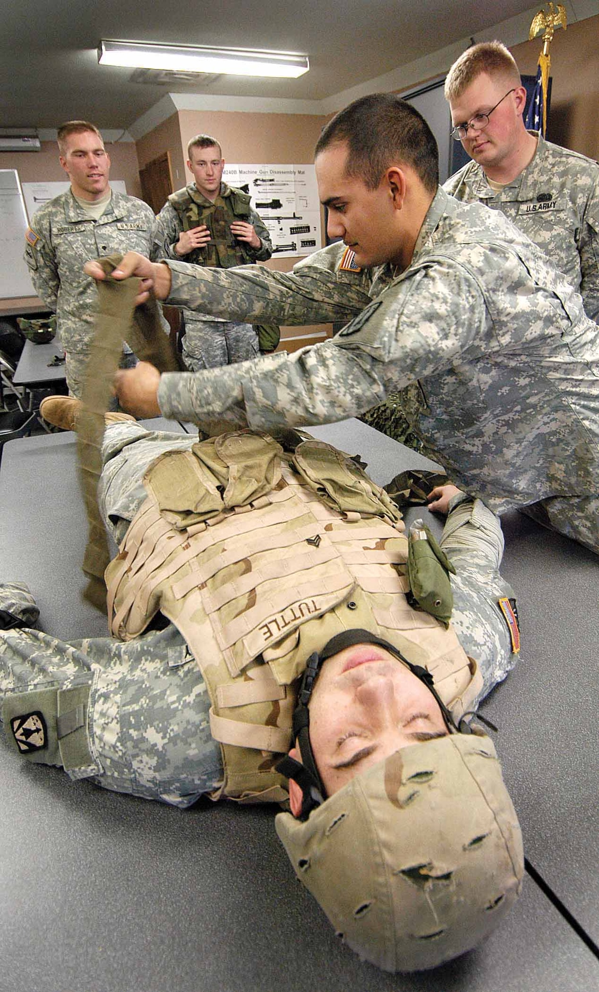 Army Pfc. Jason Scrima, Headquarters/Headquarters Battery, 6th Battalion, 52nd Air Defense Artillery, practices treating an abdominal wound after classroom training Jan. 10 at Glenwood Training Area. Sgt. Randall Tuttle acts as victim while Army medic and instructor, Sgt. Travis Melby, right, pays close attention. (Air Force photo by Margo Wright)
