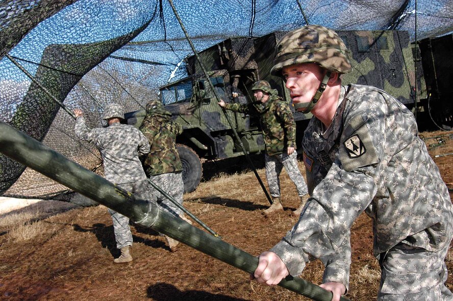 Fort Sill, Okla. Soldiers, including Spc. Daniel Graber, Headquarters/Headquarters Battery, 6th Battalion, 52nd Air Defense Artillery, raise camouflage netting over Army Tactical Control Station equipment at Tinker’s Glenwood Training Area Jan. 8.  A two-week exercise of the Army, the 3rd Combat Communications Group and the 552nd Air Control Wing showed the war-fighting advantages of joint training. ((Air Force photo by Margo Wright)
