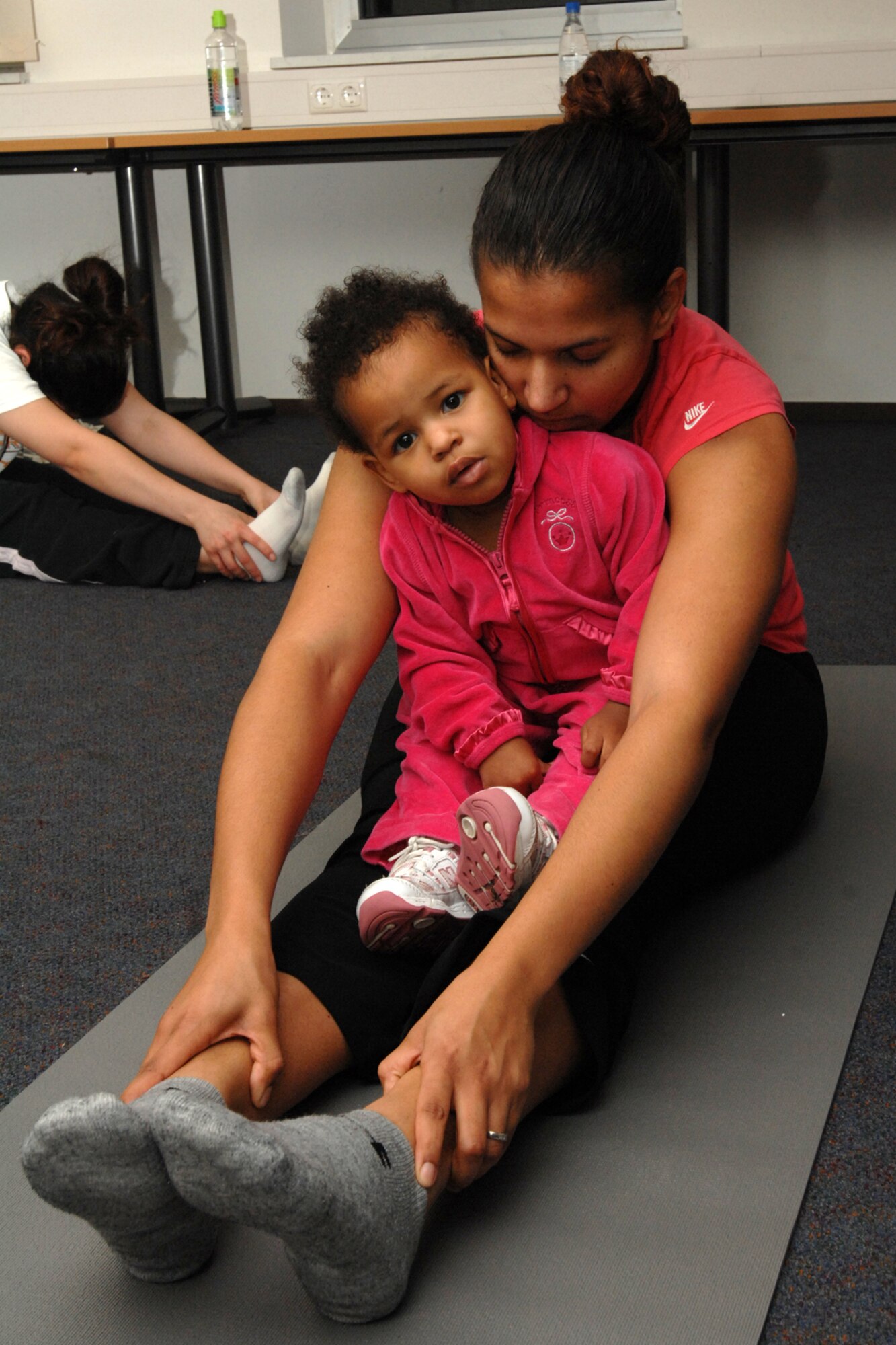 SPANGDAHLEM AIR BASE, Germany -- Tiera Harris, wife of Staff Sgt. Robert Harris, 52nd Communications Squadron, stretches while her daughter Milana, 19 months old, sits on her lap and tries to do the stretch too Jan. 17, 2008. Each week the participations of the Protestant Women of the Chapel Yoga Class receive a healthy recipe to try. (U.S. Air Force photo/Airman 1st Class Jenifer Calhoun)