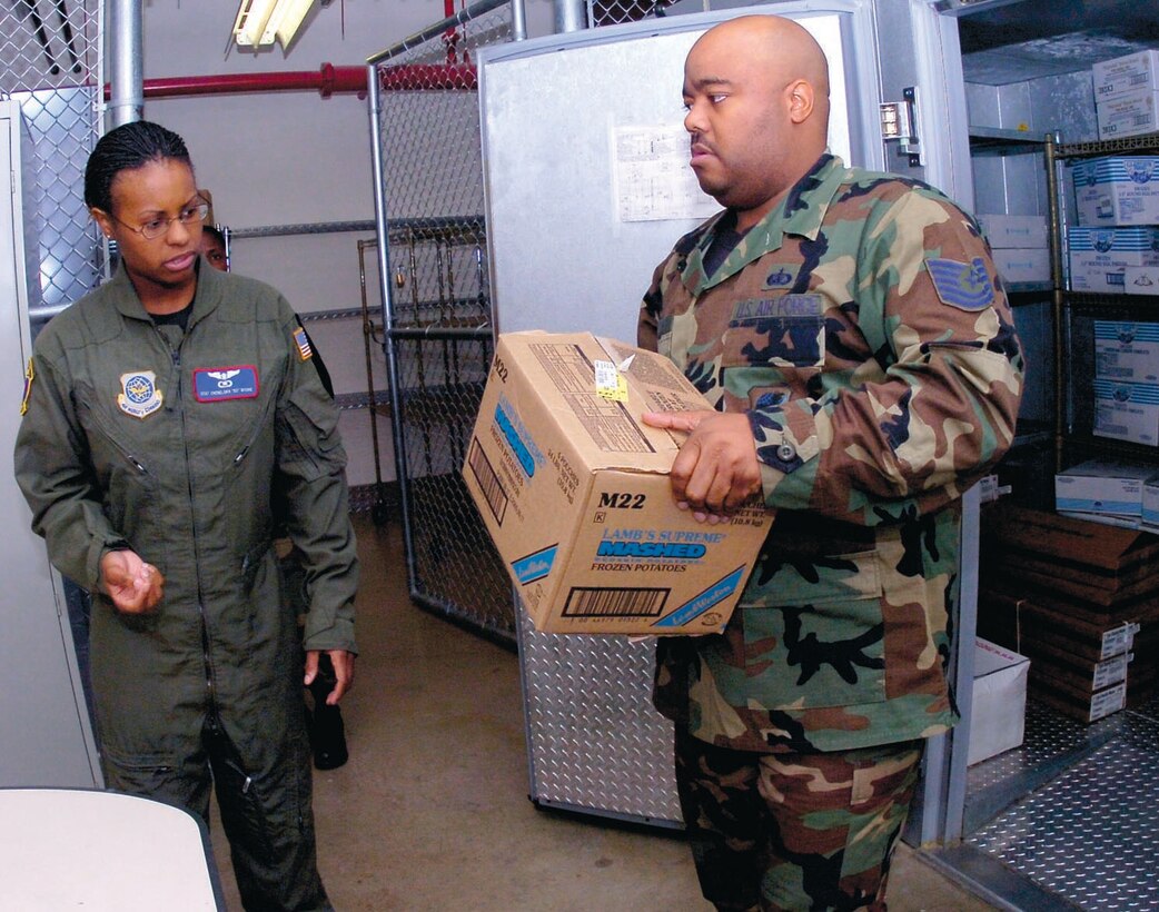 Tech. Sgt. Fred Wilson, In-Flight Service Aquisition Program, right, pulls food supplies for an upcoming mission for Staff Sgt. Cheneldra D. Moore, 1st Airlift Squadron flight attendant. (US Air Force/Bobby Jones)