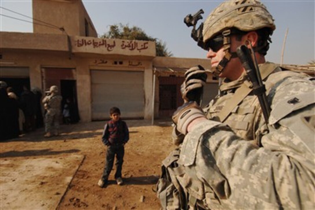 An Iraqi boy watches U.S. Army 1st Lt. Josh Jones as he radios in a situation report during a visit to local shops in Al Ja'ara, Iraq, on Jan. 14, 2008.  Jones and his fellow soldiers from Red Platoon, Baker Company, 1-15 Infantry Regiment, 3rd Heavy Brigade Combat Team, 3rd Infantry Division, are handing out applications for $2,500 micro grants in order to help shopkeepers re-establish their shops.  