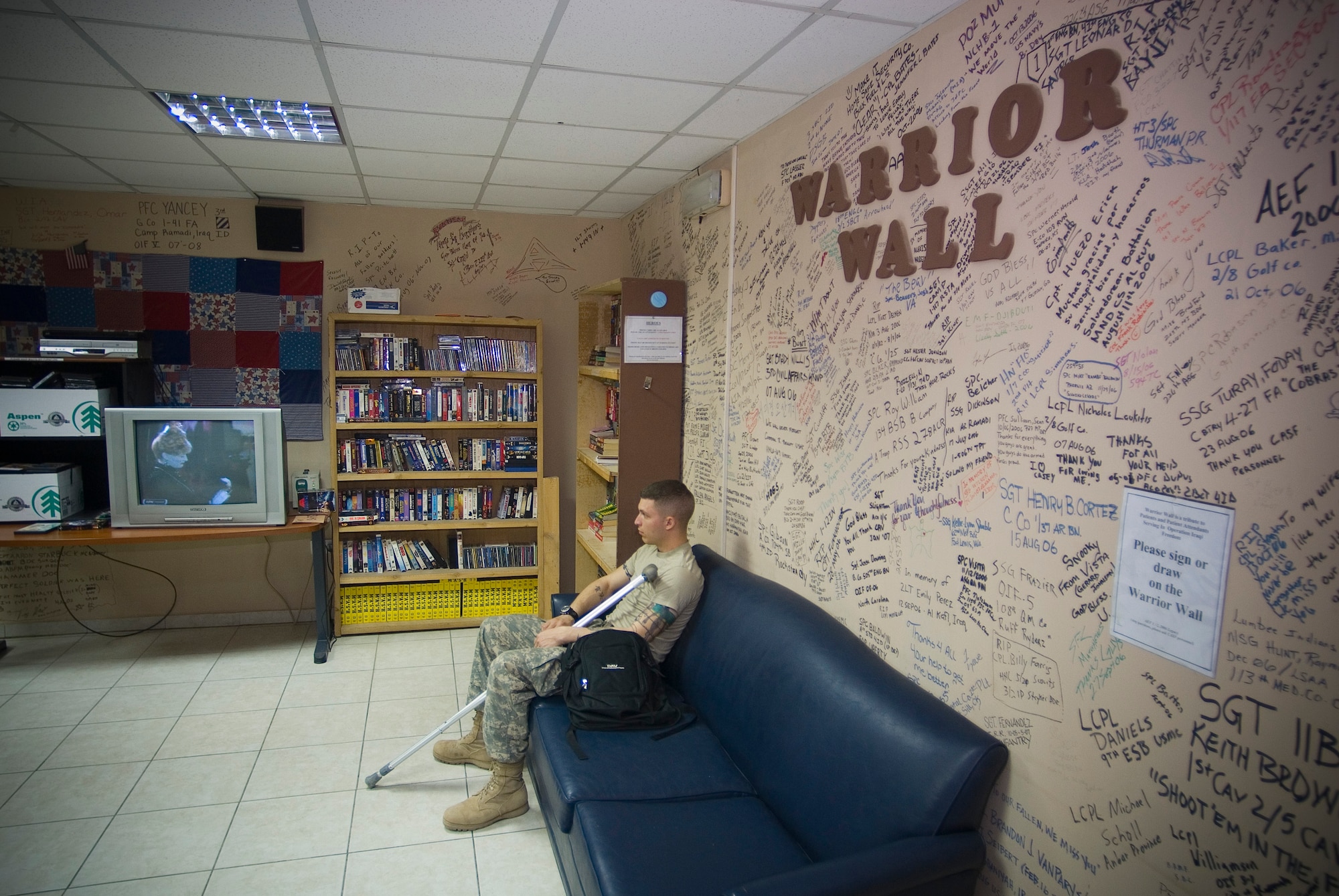 BALAD AIR BASE, Iraq -- Army Pfc. Mark W. Siegel, a combat-injured member of the 2nd Infantry Division, watches television alongside the Contingency Aeromedical Staging Facility's "Warrior Wall." The wall is decorated with signatures from past CASF patients. Private Siegel is deployed from Fort Lewis, Wash. (U.S. Air Force photo/ Master Sgt. John Nimmo, Sr.)