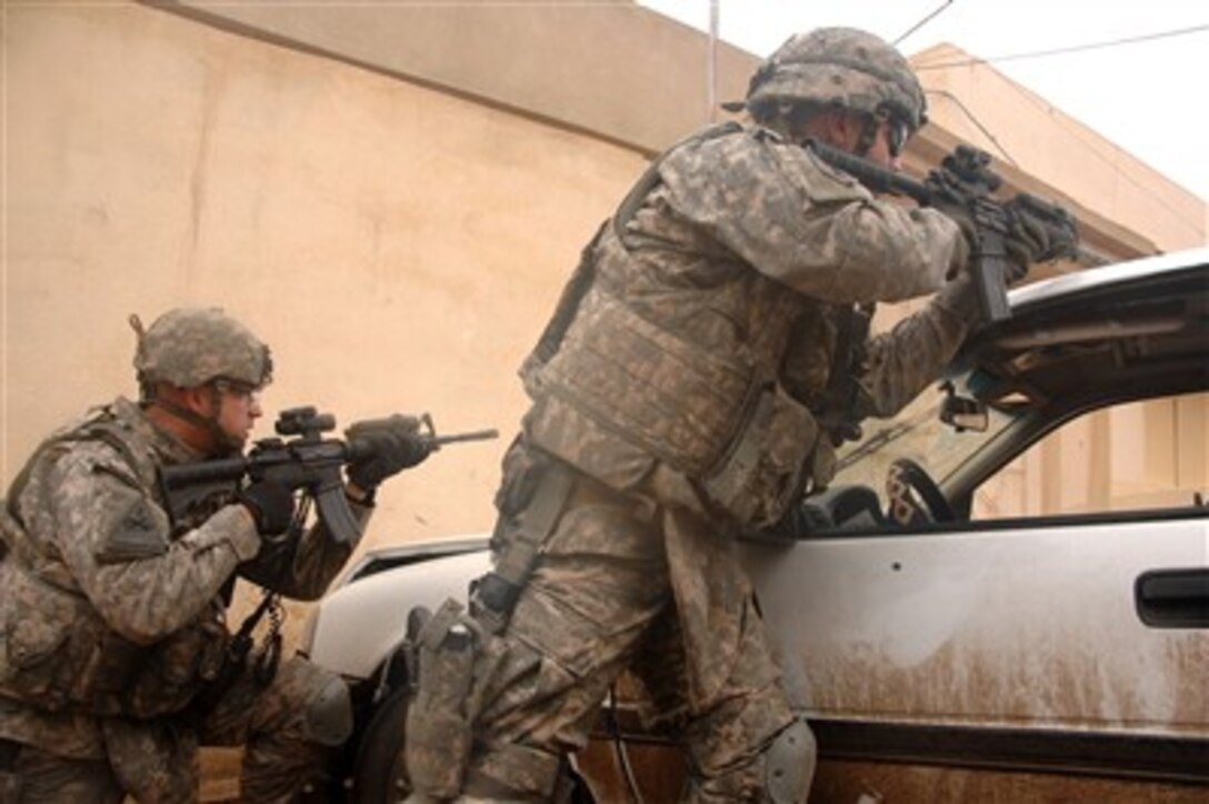Two U.S. Army soldiers take cover behind a car as they return fire during a small arms engagement in Mosul, Iraq, on Jan. 23, 2008.  The soldiers are from the military transition team assigned to 2nd Brigade, 2nd Iraqi Army Division and work side-by-side with the Iraqi Army to provide assistance and advice.  