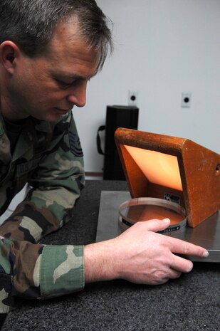 NELLIS AIR FORCE BASE, Nev.—Master Sgt. Dennis Strehlow, 57th Component Maintenance Squadron, precision measuring equipment laboratory craftsman, looks through a quartz crystal to ensure a leveling plate is free of defects here Jan. 28. The PMEL shop is responsible for making sure all equipment needed to perform Nellis' mission is correctly aligned, measured, and calibrated. (U.S. Air Force photo by Senior Airman Nadine Y. Barclay)