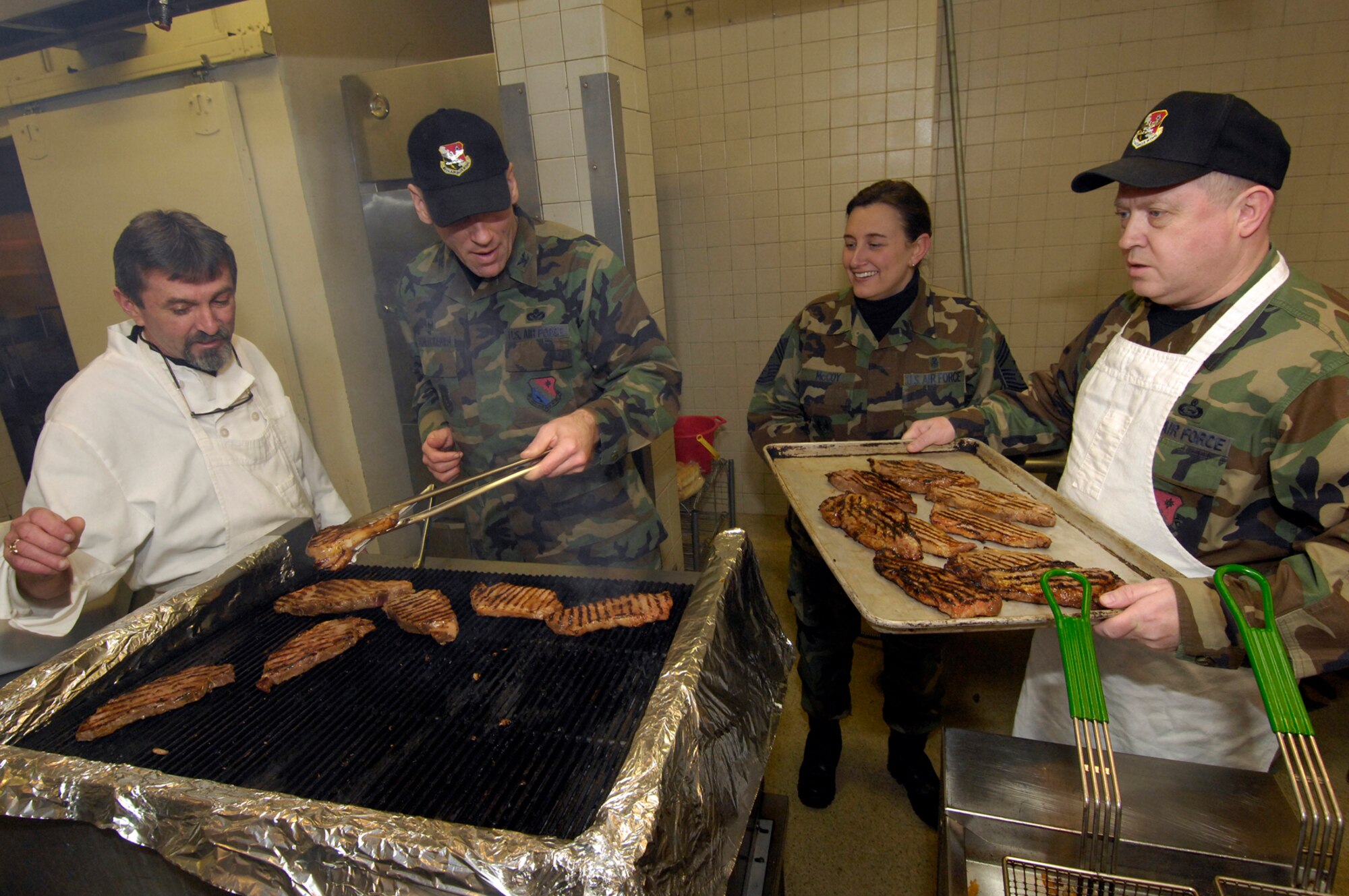 HANSCOM AFB, Mass. – The 66th Air Base Wing hosted Steak Night at the Minuteman Club Jan. 29. Pictured here from left to right, Mike Means, Minuteman Club chef, watches as Col. Tom Schluckebier, 66th Air Base Wing commander grills up the steaks and Chief Master Sgt. Karen McCoy, command chief for the Electronic Systems Center and 66 ABW, and Col. Jeff Mayo, 66 ABW vice commander prepare to serve up the grilled feast. Steak night takes place every Tuesday from 5 to 8 p.m. at the Minuteman Club. For more information on Steak Night or other Club activities call (781) 377-3799. (U.S. Air Force photo by Mark Wyatt)