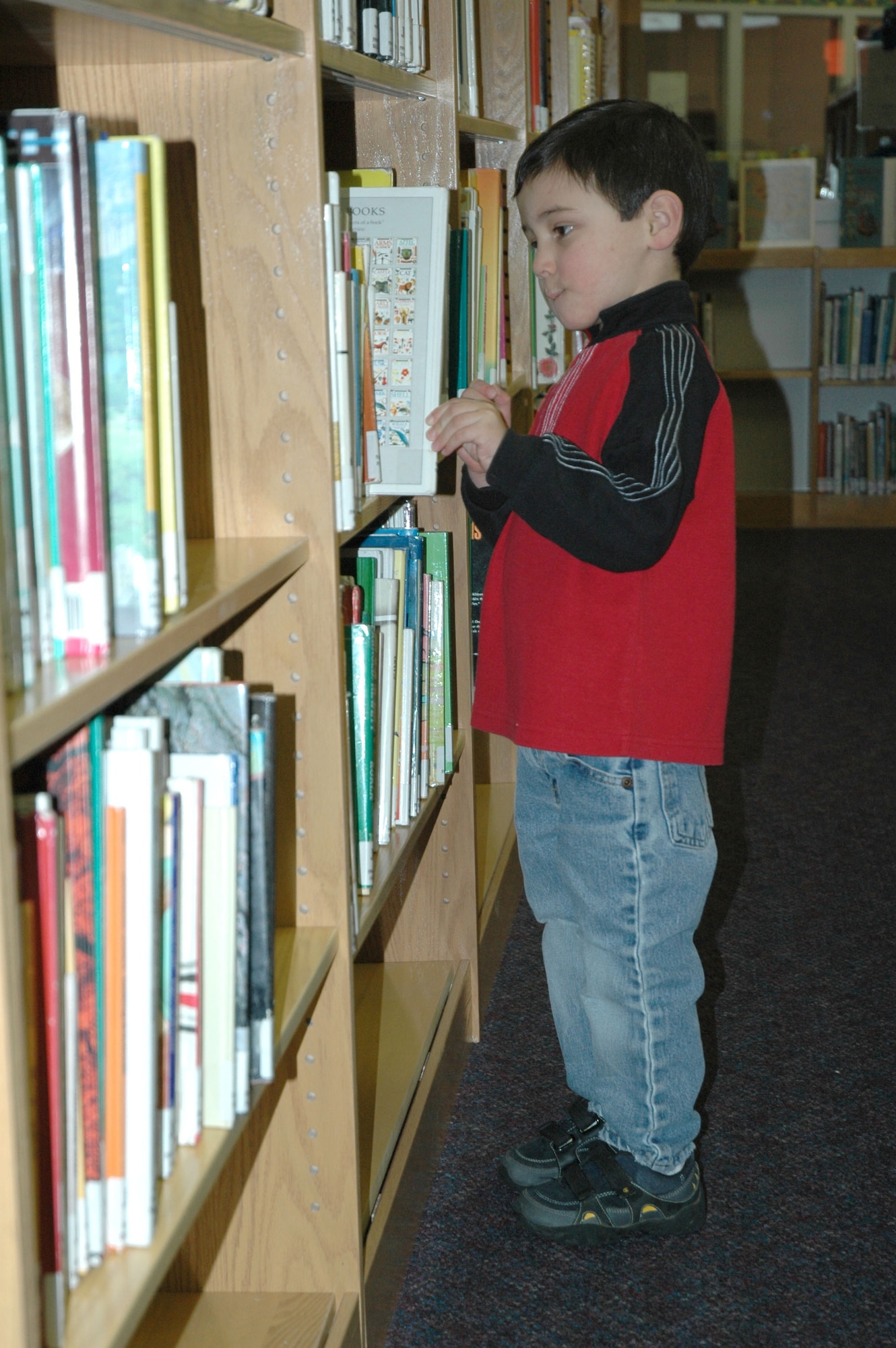 Little Warrior Joseph, 4, pulls a selection from the book racks of the Arden G. Hill Memorial Library. Joseph is a home-schooled student and was at the library collecting study materials Jan. 24. (U.S. Air Force photo/Airman 1st Class Dillon White)