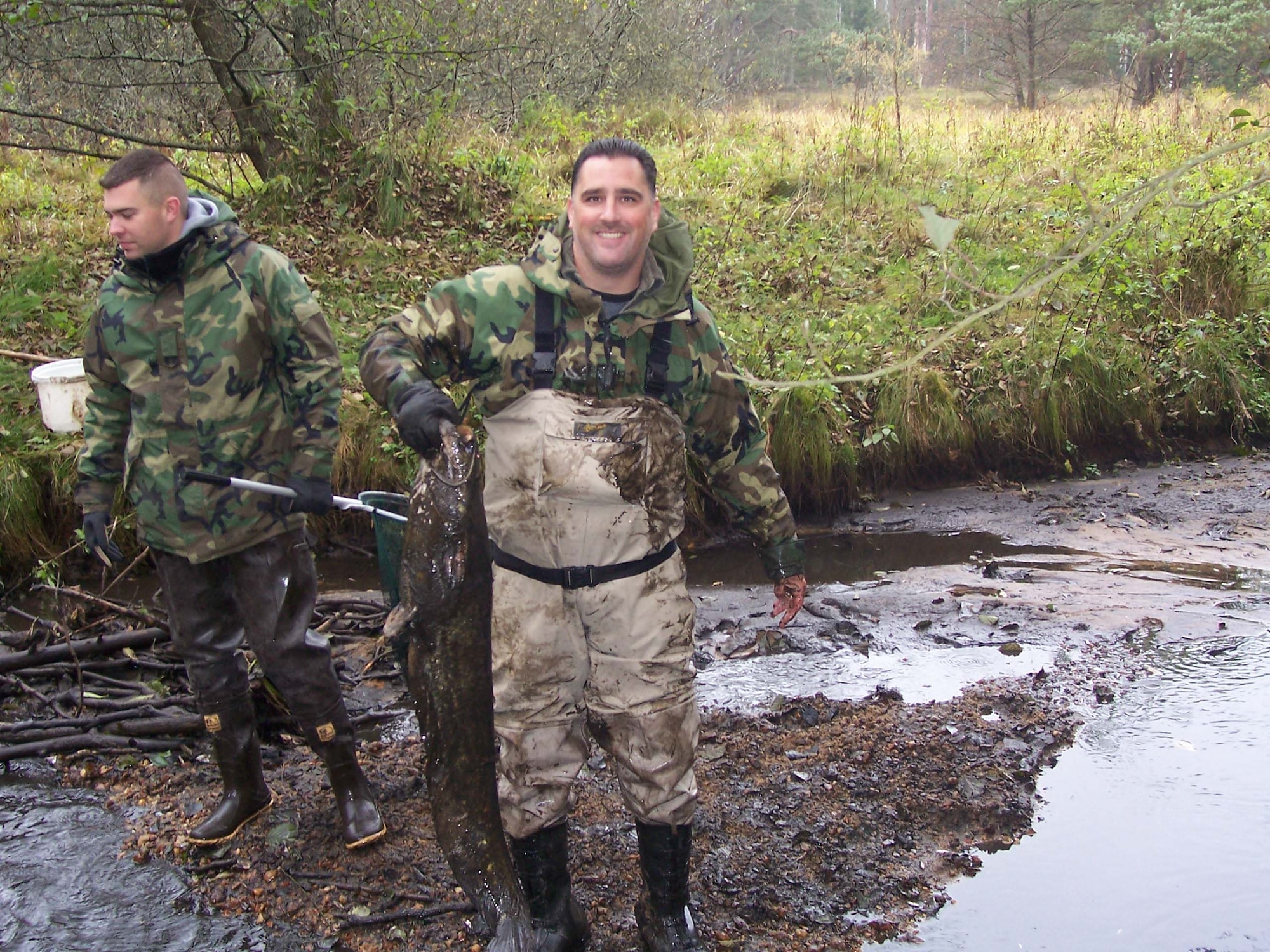 Master Sgt. Scott Windorf, 435th Munitions Squadron’s first sergeant, holds a 25-pound catfish he pulled from a log jam, while Staff Sgt. David Kieper, 435th MUNS, looks for more stranded fish. (Courtesy photo)