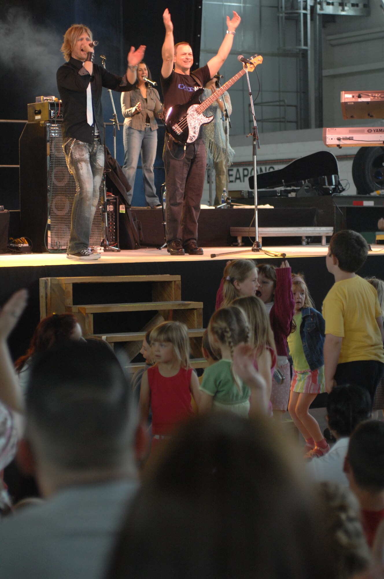 Gary Sinise, top right, plays bass guitar as Jeff Vezain, lead vocalist, top left, encourage Airmen and their families to clap along to the songs at the Lt. Dan Band concert June 29 in Hangar 539 at RAF Mildenhall. The band was here as part of a United Services Organization tour, playing to servicemembers around the world to show their support for them. Approximately 650 people watched the concert as the Lt. Dan Band interacted with the crowd and kept everyone entertained for the two-hour show. (U.S. Air Force photo by Airman 1st Class Brad Smith)