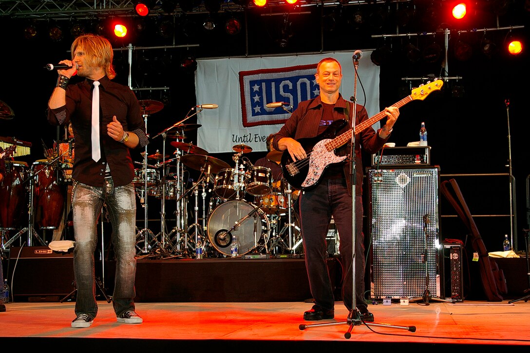 Actor Gary Sinise (right) plays bass guitar as Jeff Vezain, lead vocalist, sings to Airmen and their families at the Lt. Dan Band concert June 29 in Hangar 539 at RAF Mildenhall. The band was here as part of a United Services Organization tour, playing to servicemembers around the world to show their support for them. Approximately 650 people watched the concert as the Lt. Dan Band interacted with the crowd and kept everyone entertained for the two-hour show. (U.S. Air Force photo by Karen Abeyasekere)
