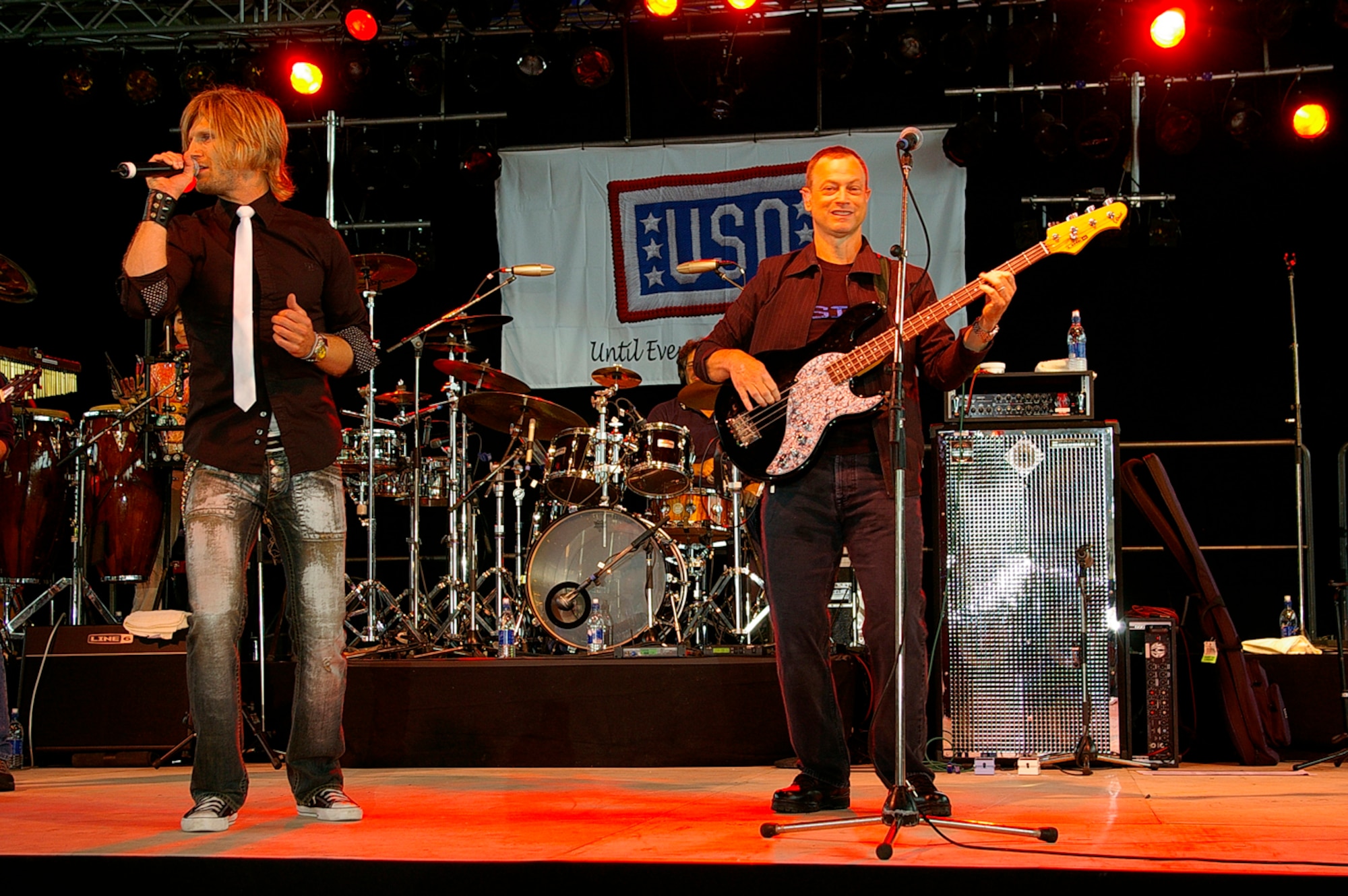 Actor Gary Sinise (right) plays bass guitar as Jeff Vezain, lead vocalist, sings to Airmen and their families at the Lt. Dan Band concert June 29 in Hangar 539 at RAF Mildenhall. The band was here as part of a United Services Organization tour, playing to servicemembers around the world to show their support for them. Approximately 650 people watched the concert as the Lt. Dan Band interacted with the crowd and kept everyone entertained for the two-hour show. (U.S. Air Force photo by Karen Abeyasekere)