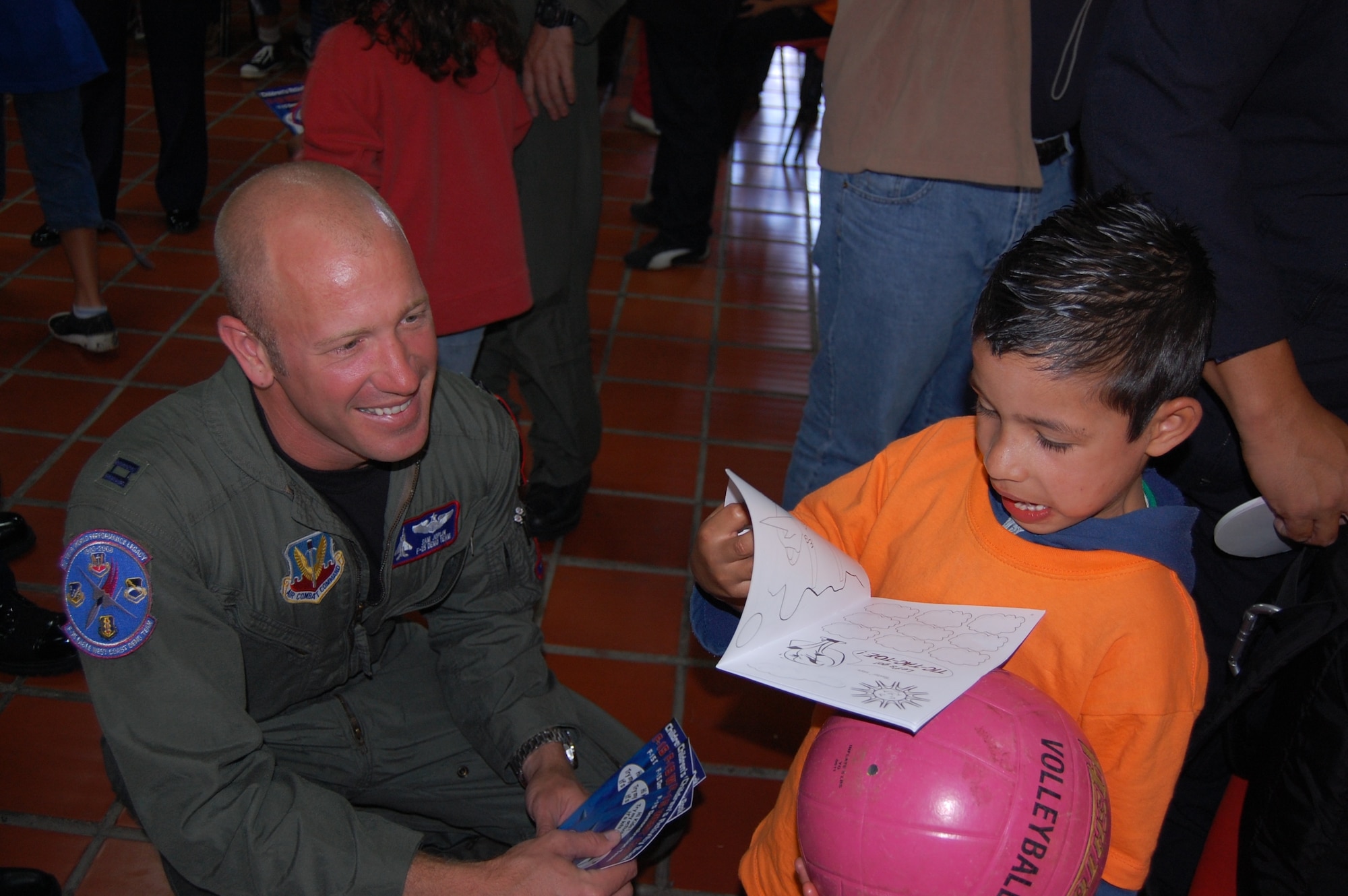 Capt. Sam Joplin, the F-15 West Coast Demonstration Team pilot, observes a child’s reaction upon receiving a coloring book from visiting Airmen.  Airmen visited and ate lunch with staff and children at the ALDEAS SOS home near Medellín, Colombia during planned community outreach events associated with the RIO NEGRO air and trade show. More than 25 Airmen gave presents of books, candy, stickers and photos to the orphans; then signed autographs and invited the group to the air and trade show the following day. (Photo by Capt. Nathan Broshear)  