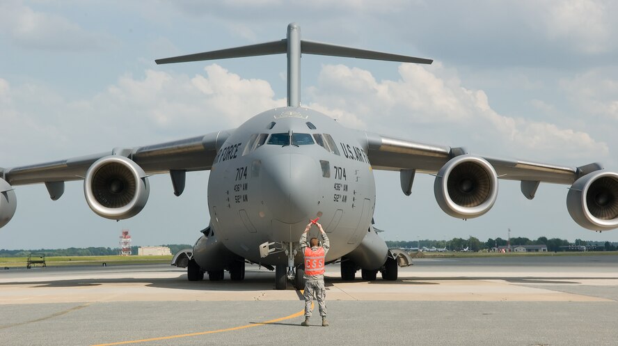 Airman 1st Class Sean Baek, 736th Aircraft Maintenance Squadron, directs the ninth C-17 Globemaster III delivered to Dover Air Force Base, Del., July 1. Brig. Gen. Brian P. Meenan, mobilization assistant to the Director of Air, Space and Information Operations, Headquarters Air Mobility Command, Scott Air Force Base, Ill., served as the delivery official. The base is scheduled to receive 13 C-17s by the end of 2008. (U.S. Air Force photo by Jason Minto)