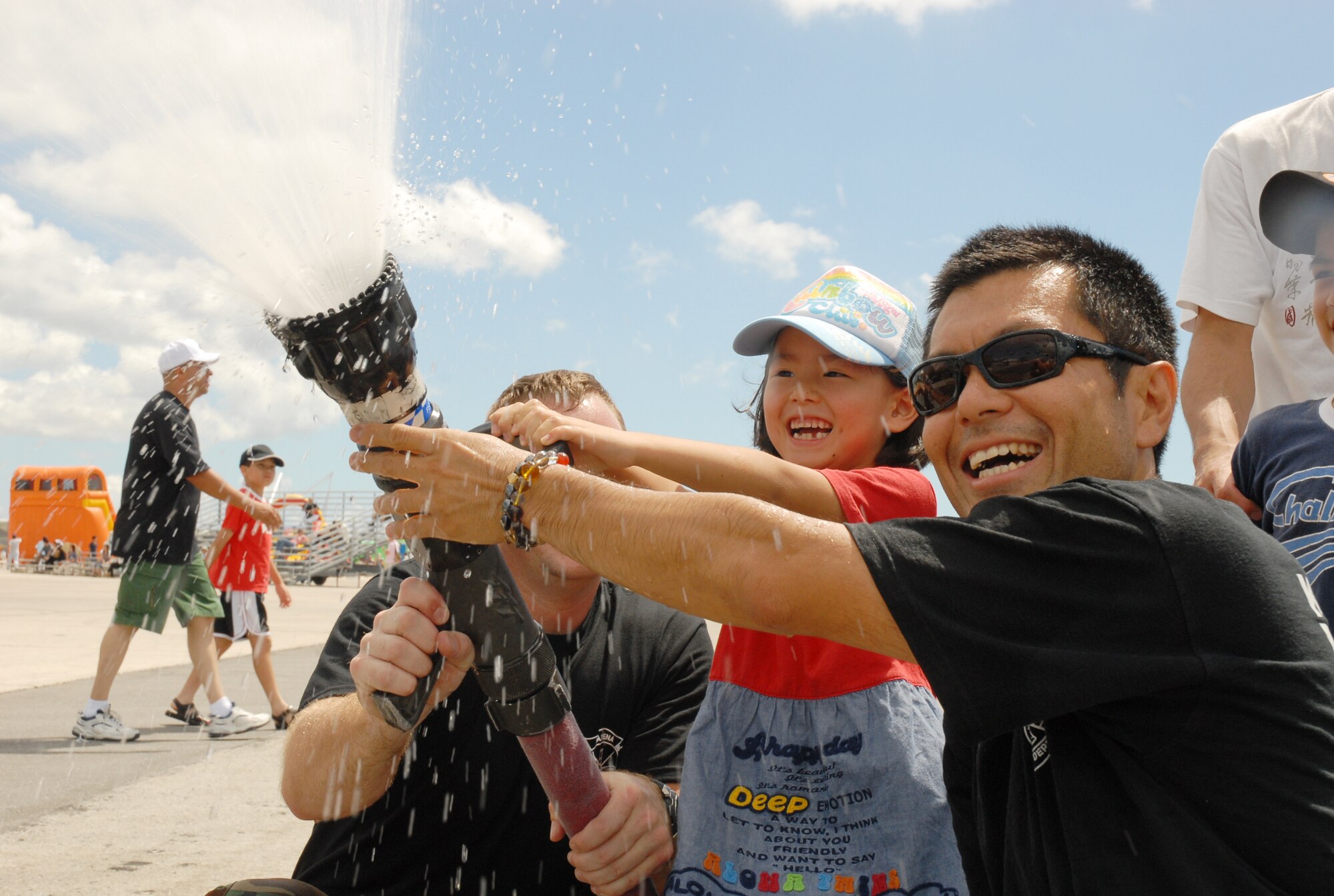 Members of the Kadena Fire Department help an Okinawan girl operate a fire hose July 5, 2008 during Kadena Air Base’s AmericaFest open house. The Fire Department was one of many units that had hands-on displays during the festival.  AmericaFest featured two dozen aircraft static displays, live entertainment, activities for children and a nightly fireworks show. The two-day event, which was designed to strengthen relations with the base's Okinawan neighbors, drew nearly 66,000 people.
(U.S. Air Force photo/Airman Chad Warren)
