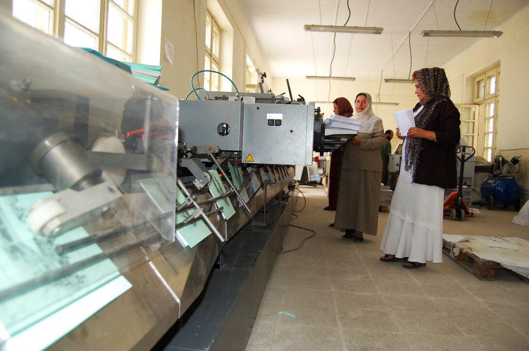 Afghan National Army civilians load lined paper into a postpress