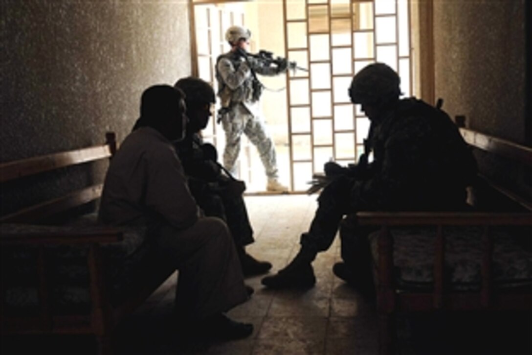 U.S. Army Staff Sgt. Jason Condreay, a military policeman, stands at the ready in providing security for U.S. Army Sgt. Michael Horst and his interpreter as they speak with the headmaster of Al-Jabar Aktar school in the Sadr City district of Baghdad, Iraq, July 2, 2008. Condreay is assigned to the 4th Infantry Division's 3rd Brigade Combat Team and Horst is assigned to the 432nd Civil Affairs Battalion.