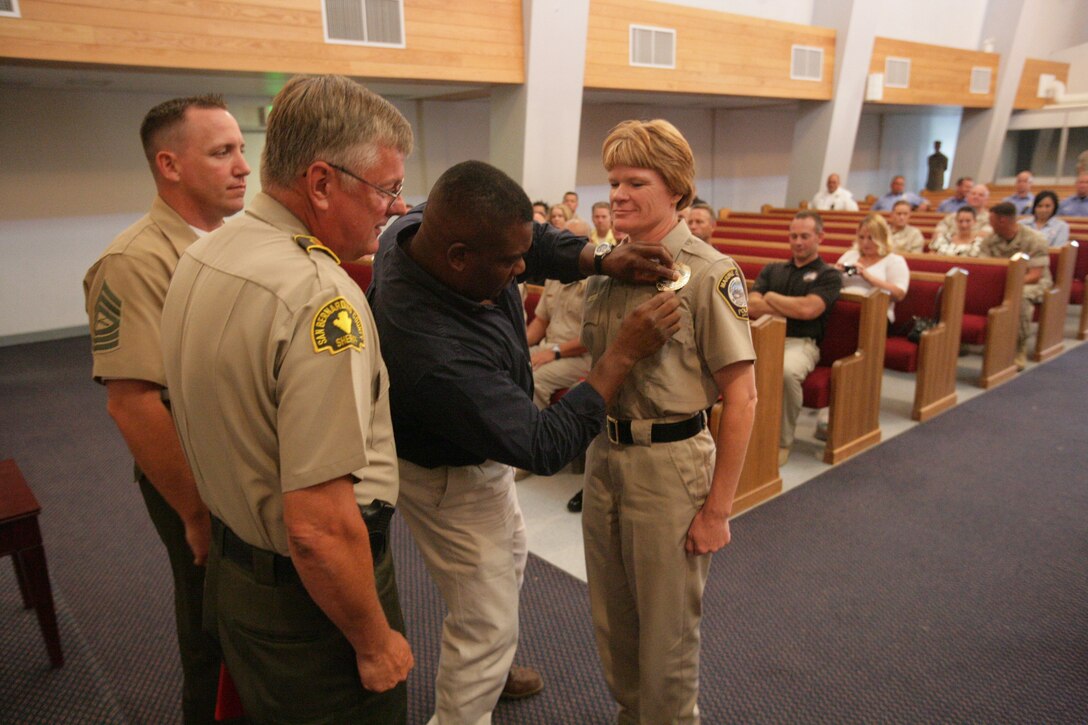 Michelle Mills, a new police officer, has her husband pin her badge on her chest during the Combat Center’s Marine Corps Police Academy graduation ceremony at the Protestant Chapel July 8, 2008.  Mills, along with her fellow civilian police officers will be the first civilians integrated into the Provost Marshal’s Office. The Combat Center will add roughly 67 civilian police officers to PMO’s ranks until fiscal year 2011, creating a gradual 50 percent conversion to civilian police officers.