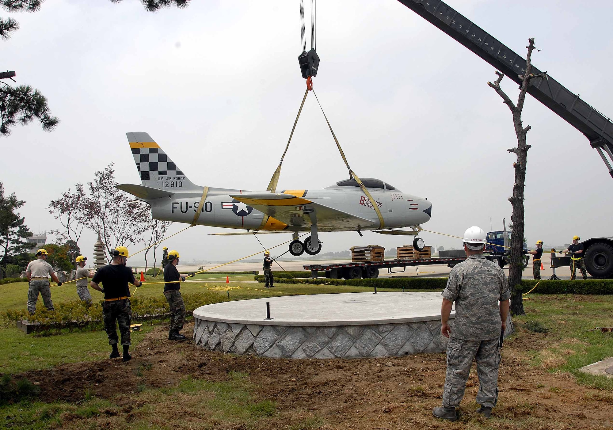 OSAN AIR BASE, Republic of Korea -- Members of the 51st Maintenance Squadron  ease a F-86 Sabre aircraft static display into its final resting place in front of base operations here July 3. The placement was the final portion of a restoration project than entailed more than 100 man-hours which included removing years of weathered paint, coatings and distinctive markings. In addition, technicians applied a weather-resistant polyurethane coating designed to protect the historic aircraft from the elements. (U.S. Air Force photo/Staff Sgt. Scottie McCord)