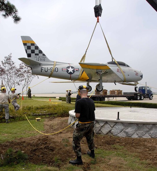 OSAN AIR BASE, Republic of Korea -- Members of the 51st Maintenance Squadron  ease a F-86 Sabre aircraft static display into its final resting place in front of base operations here July 3. The placement was the final portion of a restoration project than entailed more than 100 man-hours which included removing years of weathered paint, coatings and distinctive markings. In addition, technicians applied a weather-resistant polyurethane coating designed to protect the historic aircraft from the elements. (U.S. Air Force photo/Staff Sgt. Scottie McCord)