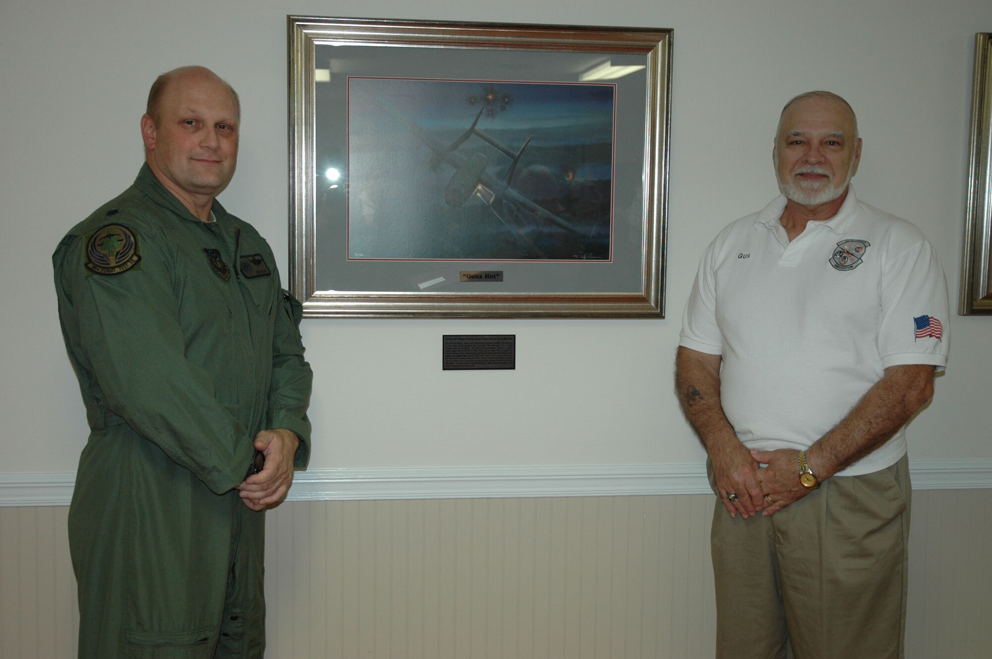 Lt. Col. Donald Peck, 18th Flight Test Squadron commander, and Gus Sininger, retired U.S. Air Force flight engineer, flank a lithograph donated to Teresa Village during a ceremony there on July 8. The original painting, by Darby Perrin, titled "Guns Hot," depicts an AC-119K Stinger gunship as it wreaks havoc on the Ho Chi Minh Trail during the Viet Nam War. The painting highlights the fifth anniversary of the AC-119 Gunship Association. Sininger was a member of the 18th Special Operations Squadron, which flew the AC-119K. The 18th FLTS has a direct lineage to the 18th SOS, and Colonel Peck took a special interest in the AC-119 gunship and its history. (U.S. Air Photo by Master Sgt. Buffy Galbraith)