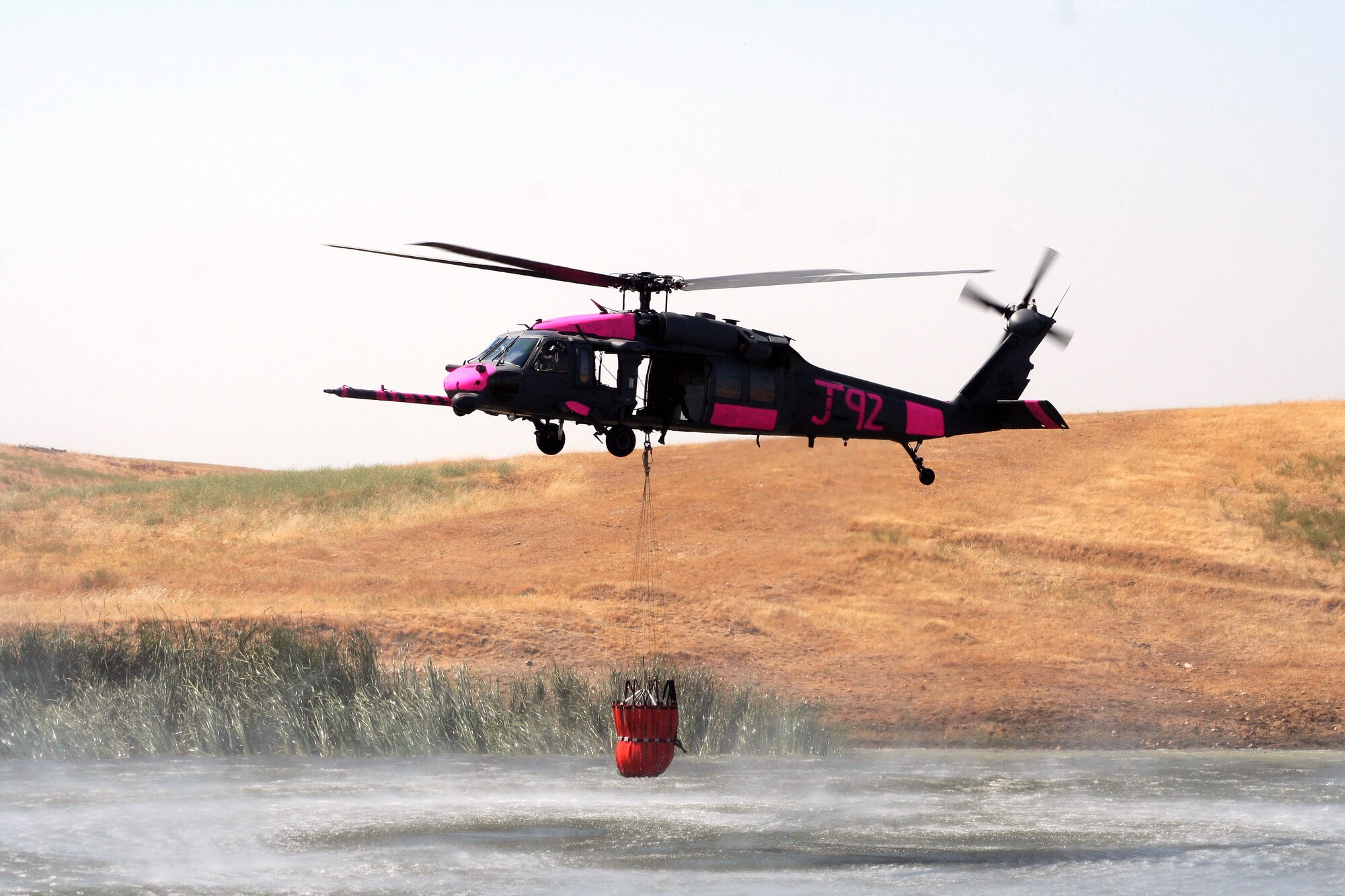 An HH-60G Pave Hawk hovers over a pond July 2 near Sacramento, Calif. The aircrews trained with water buckets to become certified for firefighting suppression duty. The HH-60G is from the 129th Rescue Wing of the California Air National Guard. (U.S. Air Force photo/Master Sgt. Barbara Apkarian) 
