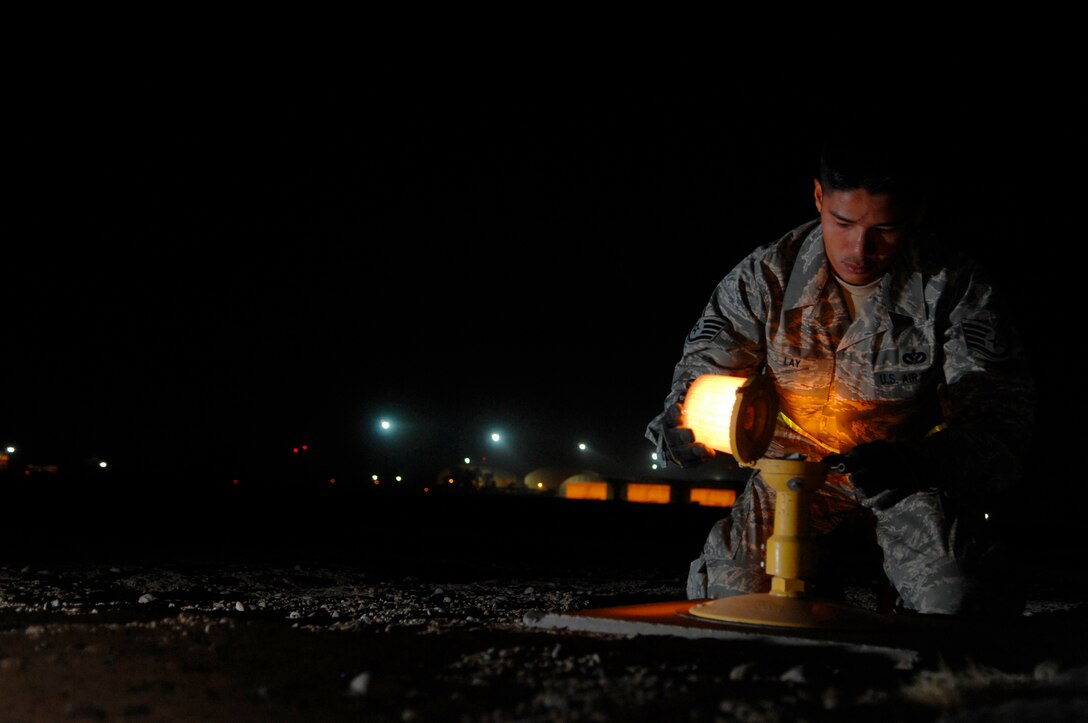 JOINT BASE BALAD, Iraq -- Staff Sgt. Samnang Lay, 332nd Expeditionary Civil Engineer Squadron electrician, replaces a bulb on a runway edge light here, July 5. The airfield lights safely guide aircraft during taxi, take off and landing during inclement weather and nighttime operations. Sergeant Lay is deployed from Ellsworth Air Force Base, S.D. (U.S. Air Force photo/ Senior Airman Julianne Showalter)