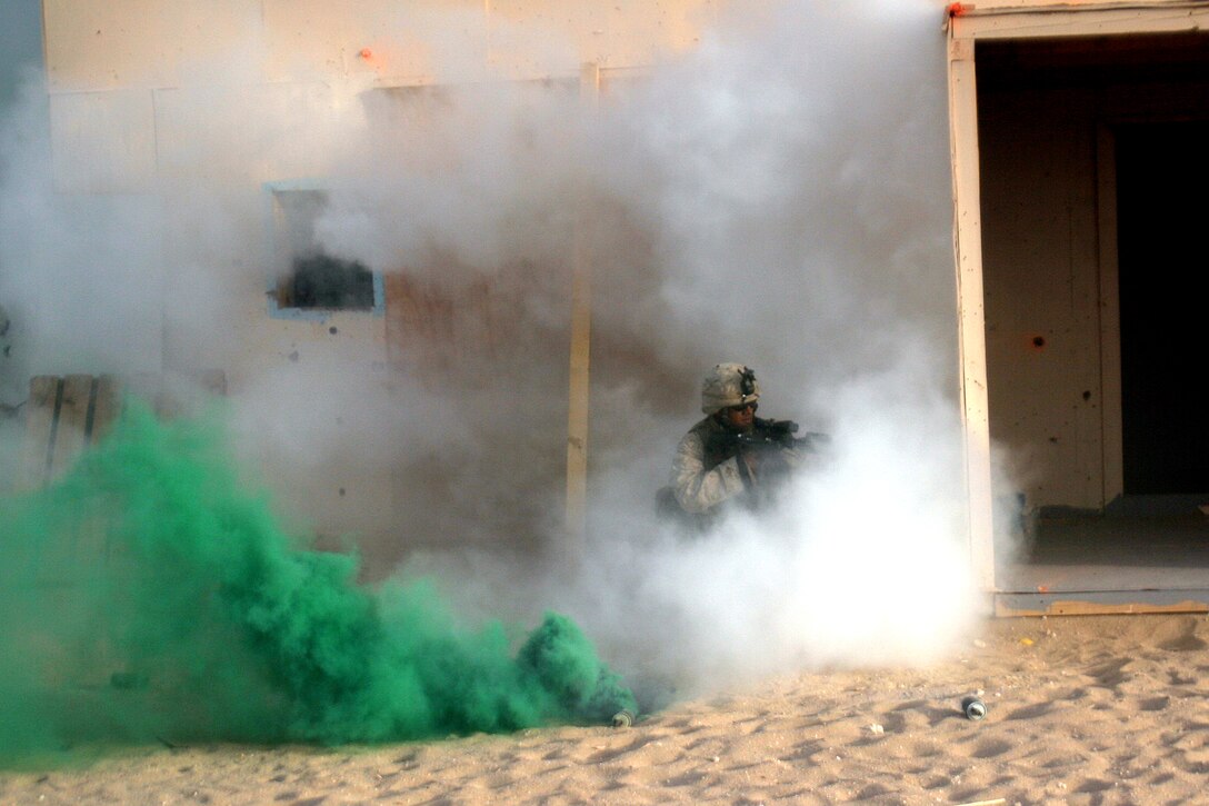 Concealed in smoke during a live-fire, urban-terrain exercise, Lance Cpl. Randy Aisen, a light-armored vehicle scout, provides cover while his team members place a breach charge. Aisen serves with Weapons Company, Battalion Landing Team 2/5, 15th Marine Expeditionary Unit, which came ashore to Kuwait in late June to conduct sustainment training in the north.