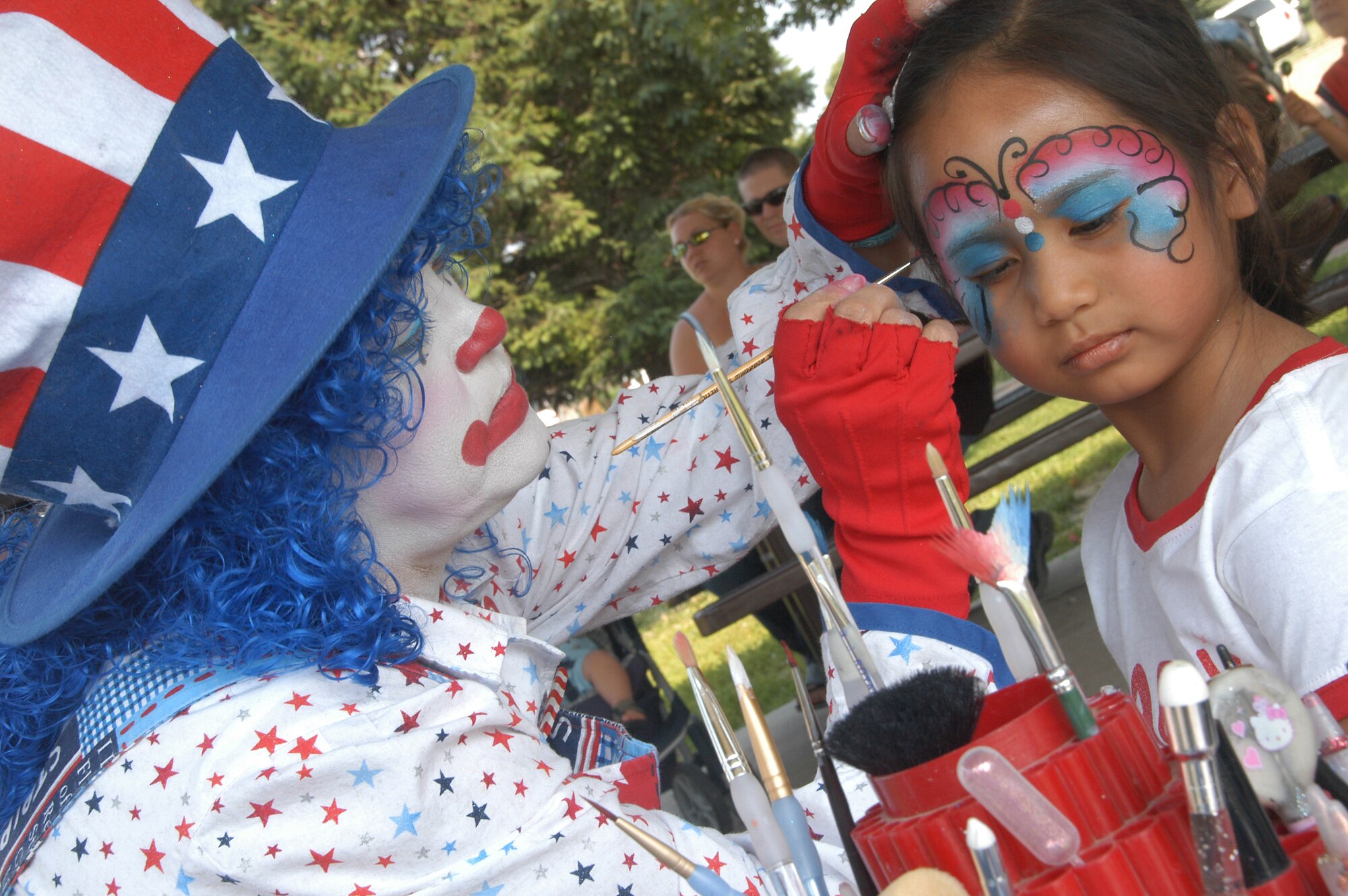 Cassandra Rodriguez, daughter of Tech. Sgt. Carlos Naok, has her face painted by Rainbow Trout the clown at the Base Lake as part of Offutt’s Family Adventure Jamboree July 4. (U.S. Air Force Photo By/Jeff Gates)