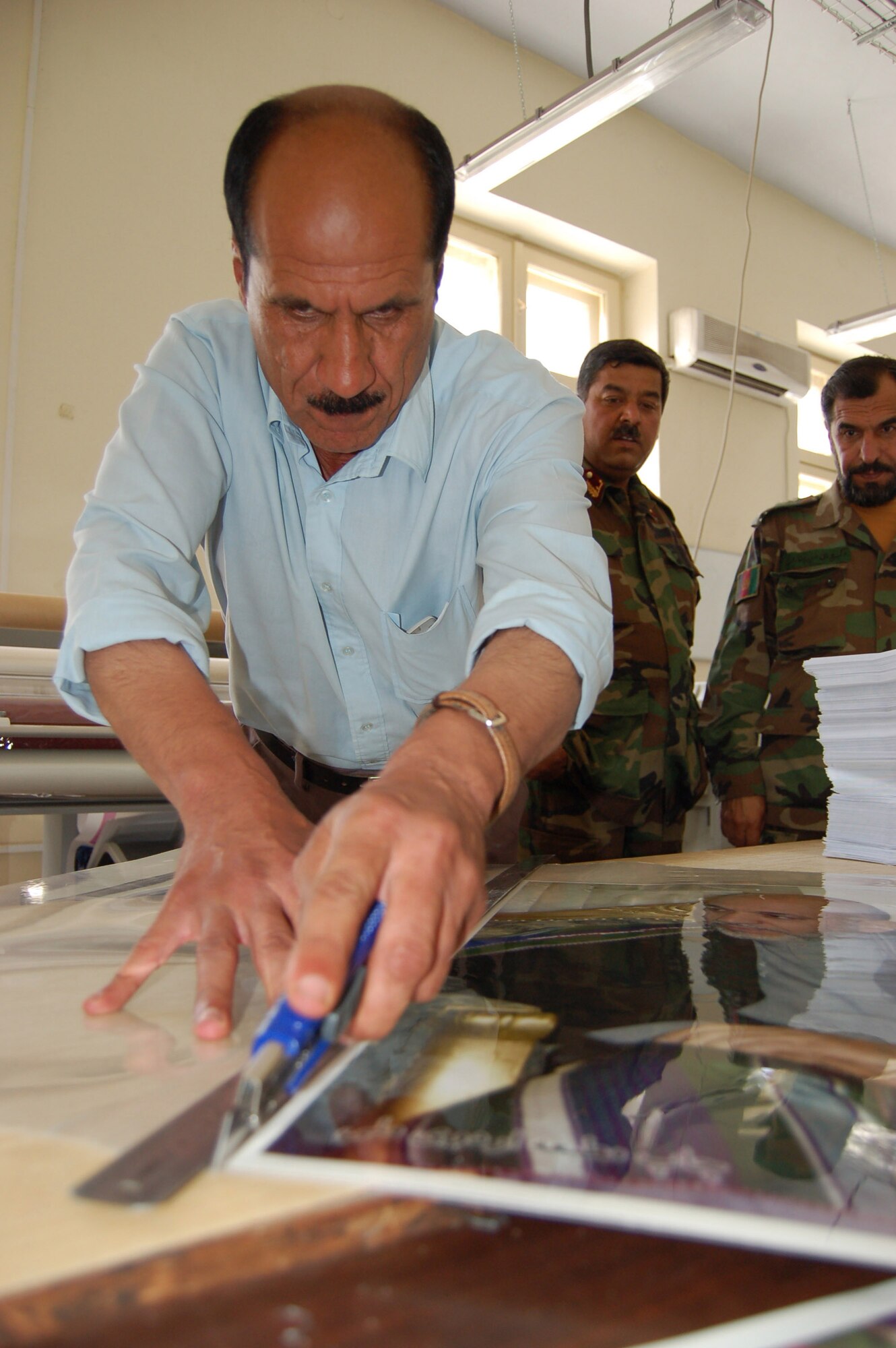 An Afghan National Army civilian cuts the laminate on a poster at the ANA print plant in Kabul, Afghanistan. During an average week, the plant produces more than 75,000 products used for training, recruitment and logistical support. (U.S. Air Force photo/Staff Sgt. Beth Del Vecchio)