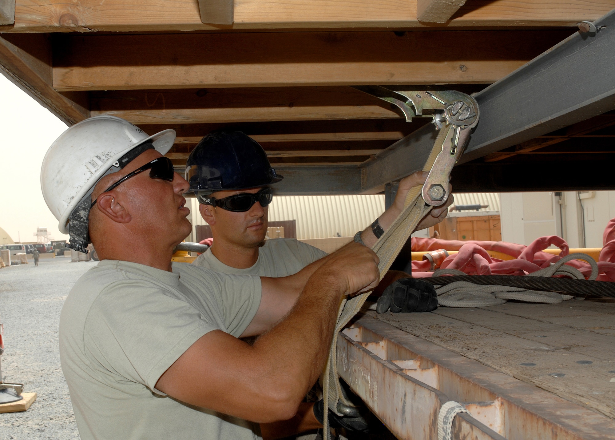 SOUTHWEST ASIA -- Senior Master Sgt. Raymond Yurista, left, and Staff Sgt. Chris Isbell, both members deployed to the 386th Expeditionary Civil Engineer Squadron, use cargo straps to secure a trailer to a flatbed truck on July 9 at a base in Southwest Asia. The trailer is being moved to the 386th Expeditionary Security Forces Squadron K-9 area to increase the square footage of the facility. Sergeant Yurista is deployed from the 201st Red Horse Squadron, Fort Indiantown Gap, Pa. Sergeant Isbell is deployed from the Utah Air National Guard. (U.S. Air Force photo/Tech. Sgt. Raheem Moore)