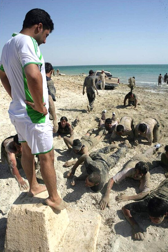 An Iraqi instructor stands atop a cement block and looks on as members of the Iraqi Special Weapons and Tactics team crawl toward it on a beach at Lake Quadsiyah in Haditha, Iraq, July 7, 2008. 