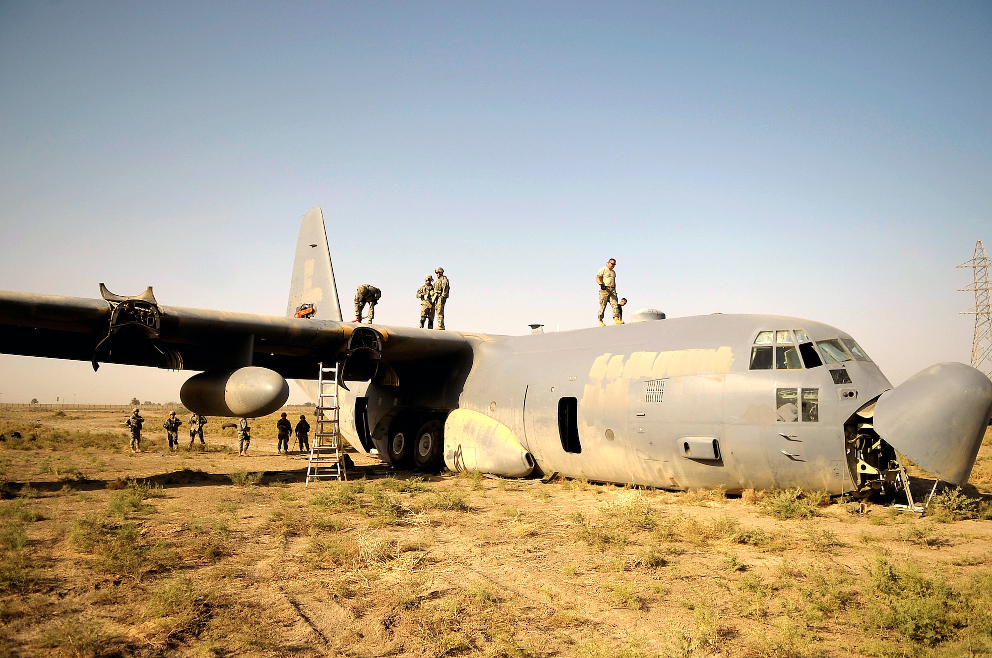 Maintenance and explosive ordnance disposal personnel from the 447th Air Expeditionary Group prepare to place explosive charges on the wings of a C-130 Hercules aircraft that are designed to divide the plane into smaller sections so it can be moved July 7 in Baghdad, Iraq. The C-130 made an emergency landing in a field north of the Baghdad International Airport shortly after take-off on June 27. (U.S. Air Force photo/Tech. Sgt. Jeffrey Allen)
