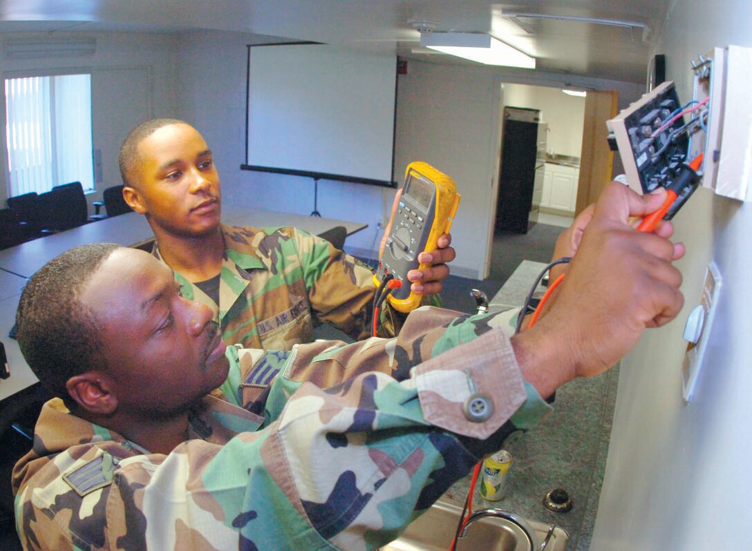 Senior Airman Alfonso Reed, 316 CES supervisor, shows Airman Robert Stocke, 316 CES HVAC apprentice, how to properly check a thermastat using a voltagemeter at Building 1602. (US Air Force/Bobby Jones)