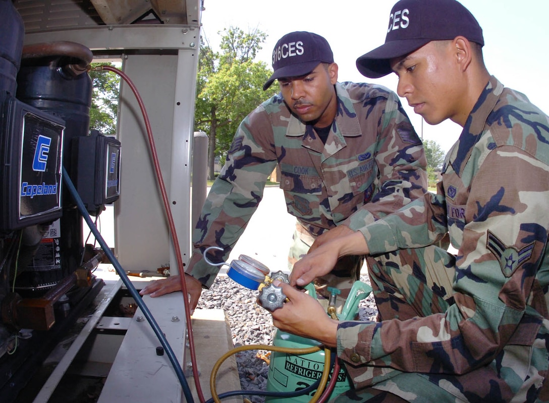 Staff Sgt. Darren Cook, 316 CES HVAC craftsman, left, teaches Airman 1st Class Brett Elan, 316 CES apprentice, how to properly charge an air conditioning chiller with refrigerant and manifold gauges outside the Squadron Operations Building.(US Air Force/Bobby Jones)