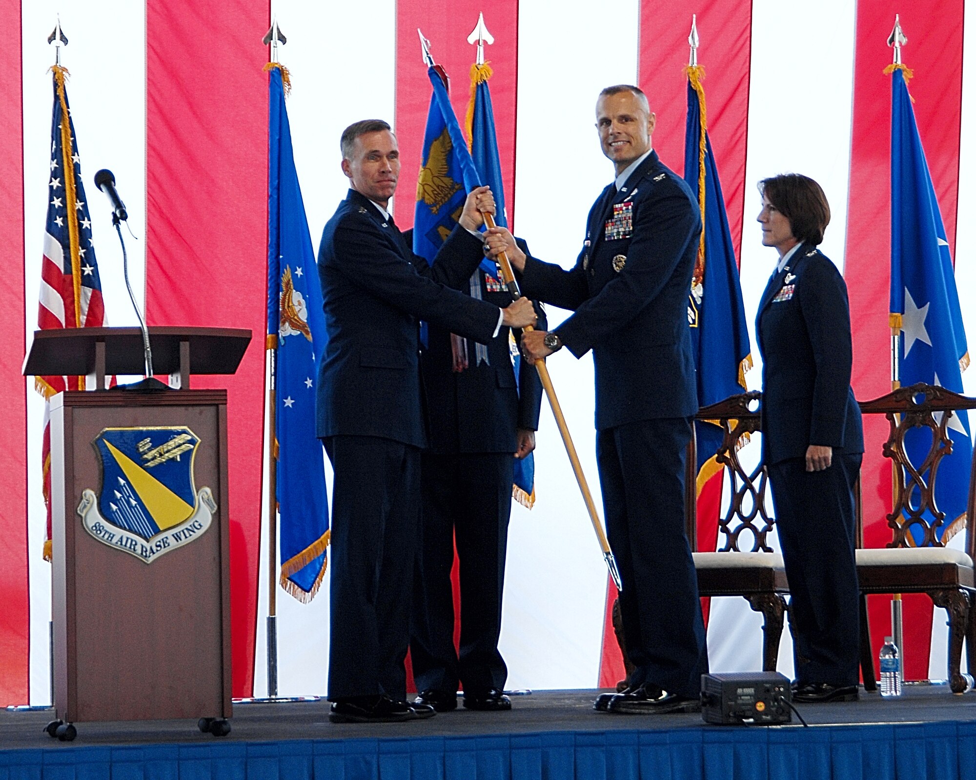 Lt. Gen. Jack Hudson, Aeronautical Systems Center commander, passes the colors for the 88th Air Base Wing to Col. Bradley D. Spacy, during a change of command ceremony in Hangar 206 at Wright-Patterson Air Force Base, Ohio July 14.  Colonel Spacy, a career Security Forces officer,  succeeded Col. Colleen Ryan (right), who is retiring. (U.S. Air Force photo/Ben Strasser).