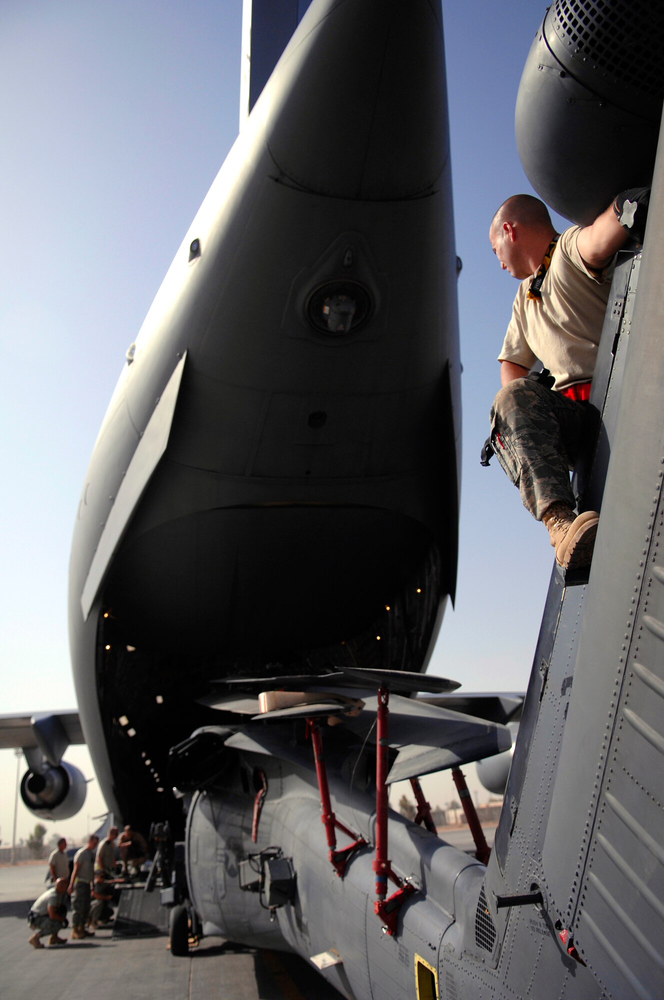 JOINT BASE BALAD, Iraq -- Staff Sgt. Joshua Sallander, 64th Expeditionary Helicopter Maintenance Unit crew chief, sits on the tail rotor of an HH-60 Pave Hawk while it's loaded onto a C-17 Globemaster III here July 12. Positioning several Airmen around and on the helicopter ensures it will not make contact with the aircraft and cause damage. The HH-60 is in a folded configuration to better fit into the C-17. Sergeant Sallander is deployed from Davis-Monthan Air Force Base, Ariz. (U.S. Air Force photo/Senior Airman Julianne Showalter) 