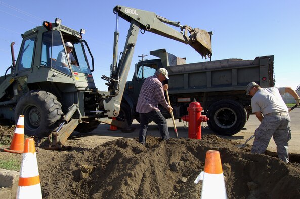 MINOT AIR FORCE BASE, ND -- Staff Sgt. Neil Crawn, 5th Civil Engineer Squadron heavy equipment operator, works alongside Wayne Kabanuck as they level fresh ground dug up by equipment operator Joe Walkup here July 14. The crew is putting in a curb around a newly replaced fire hydrant near the Base Exchange. The 5th CES is keeping busy around base this summer working on base upkeep and new construction projects. (U.S. Air Force photo by Senior Airman Kelly Timney)
