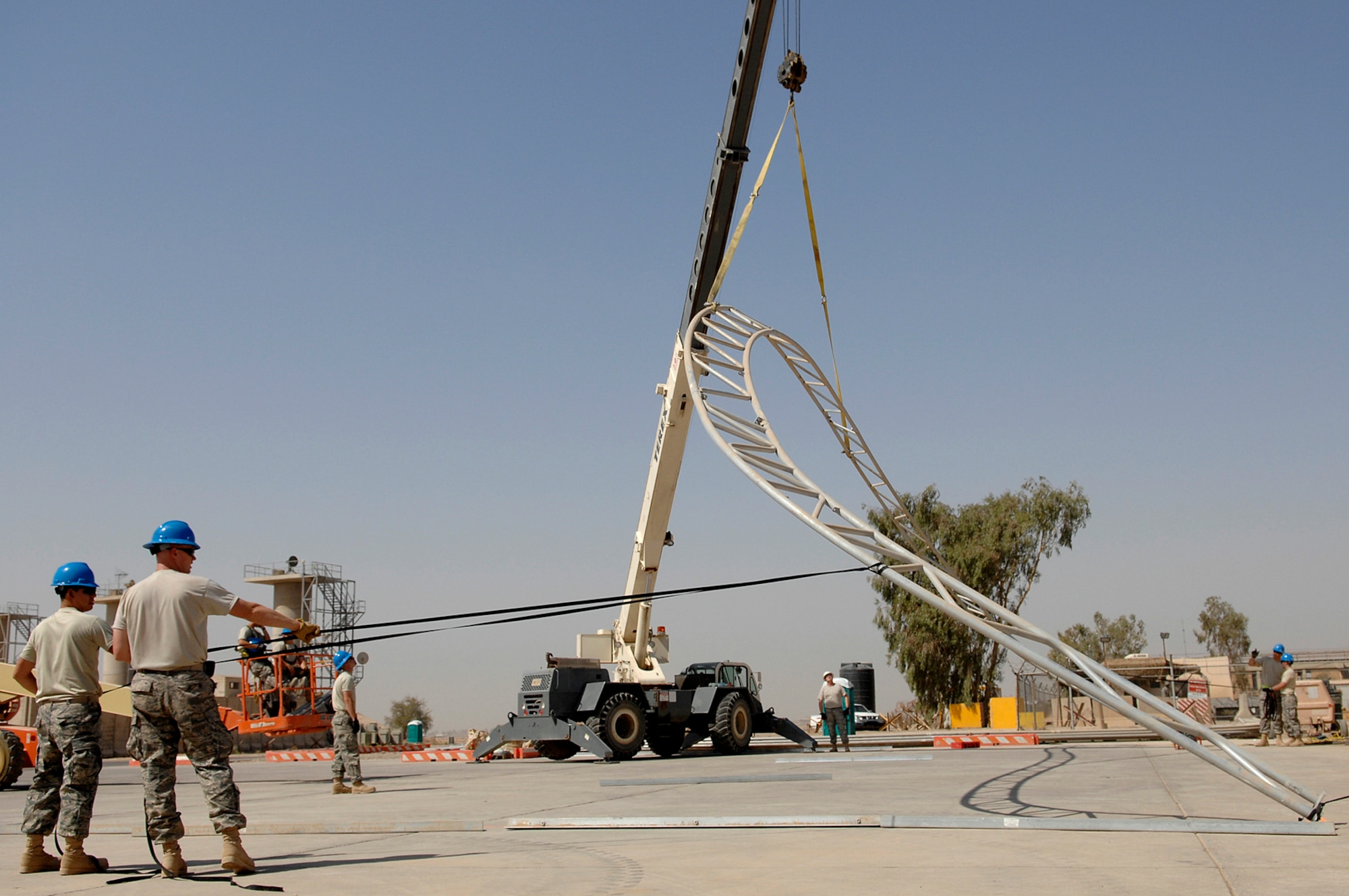 JOINT BASE BALAD, Iraq -- Airman 1st Class Brandon Trujillo and Staff Sgt. Brian Hanke, 332nd Expeditionary Civil Engineer Squadron "Dirt Boyz", hold tether ropers as one of the arches for a sun shade is positioned here July 15. Six arches make up the assembly and will be used to shield light fixed-wing aircraft from the summer sun. Airman Trujillo and Sergeant Hanke are deployed from Cannon Air Force Base, N.M. (U.S. Air Force photo/Senior Airman Julianne Showalter)