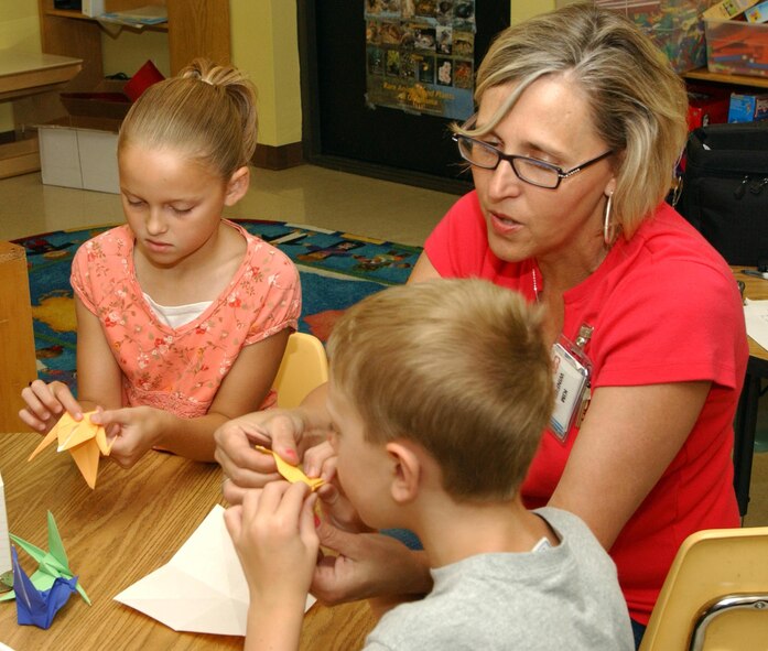 Taylor McClelland and Sam Keith gather around Kim Winfield, School Age Coordinator, to watch her demonstrate how to fold paper cranes at the Vance Air Force Base Youth Center, Okla. The cranes are part of the Hope Box project, a program founded by the Oklahoma Memorial Foundation to teach about the effects of discrimination. (U.S. Air Force photo by Stephen Fuller)