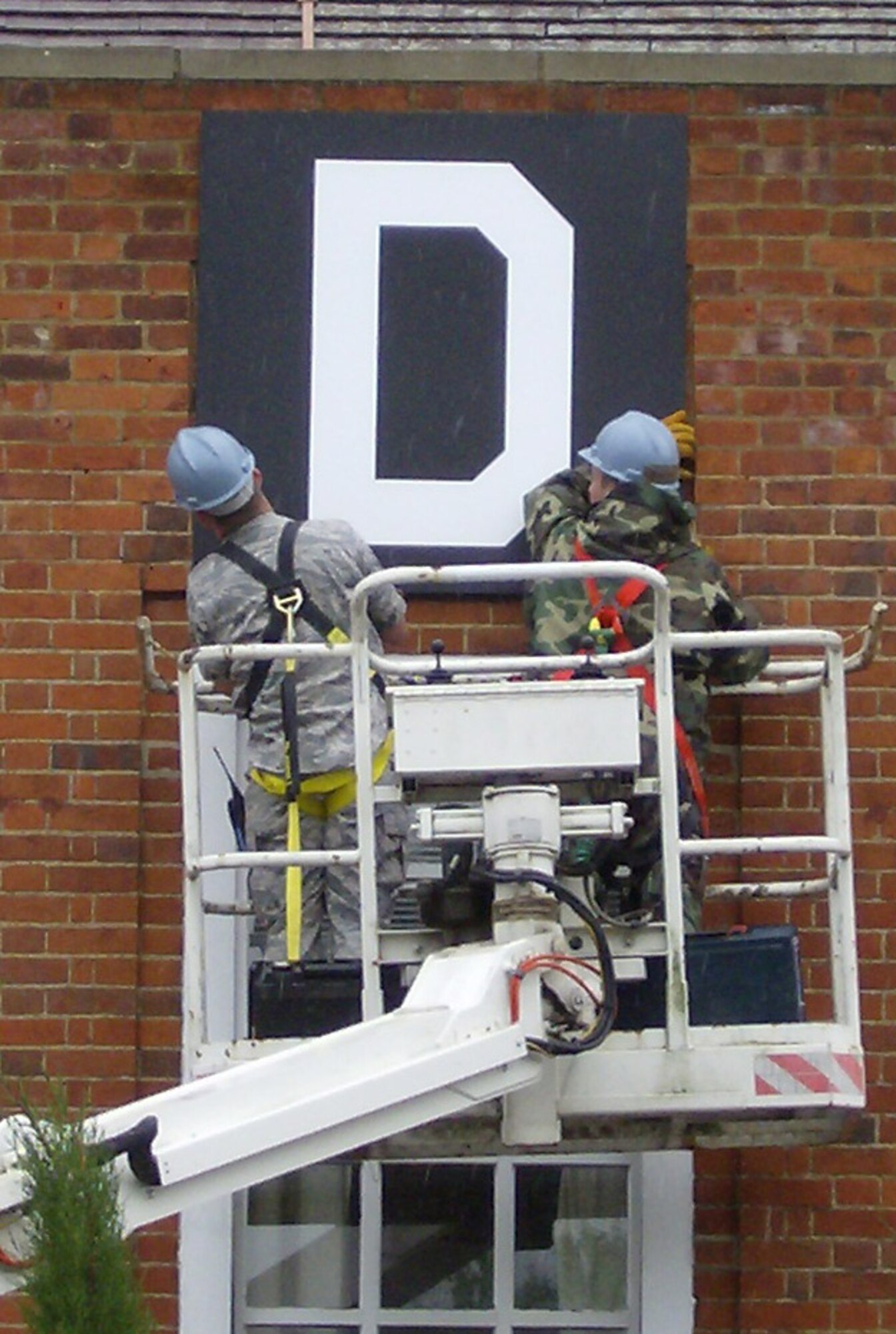 RAF MILDENHALL, England -- Airman 1st Class Andrew Rossman and Airman Scott Ricketts, 100th Civil Engineer Squadron, tighten the final bolts of the legacy "Square D" emblem to the brickwork on Bldg. 239. The "Square D" dates back to the 100th Air Refueling Wing heritage unit, the 100th Bomb Group, during World War II. (U.S. Air Force photo by John Williamson)