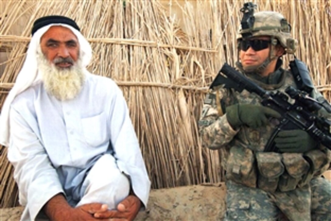 U.S. Army Staff Sgt. Esteban Vazquez takes a break to sit next to an Iraqi man while maintaining a nearby security checkpoint in Sadr Yusifiyah, Iraq, July 12, 2008. Vazquez is assigned to the 101st Airborne Division, 1-187 Infantry Regiment.