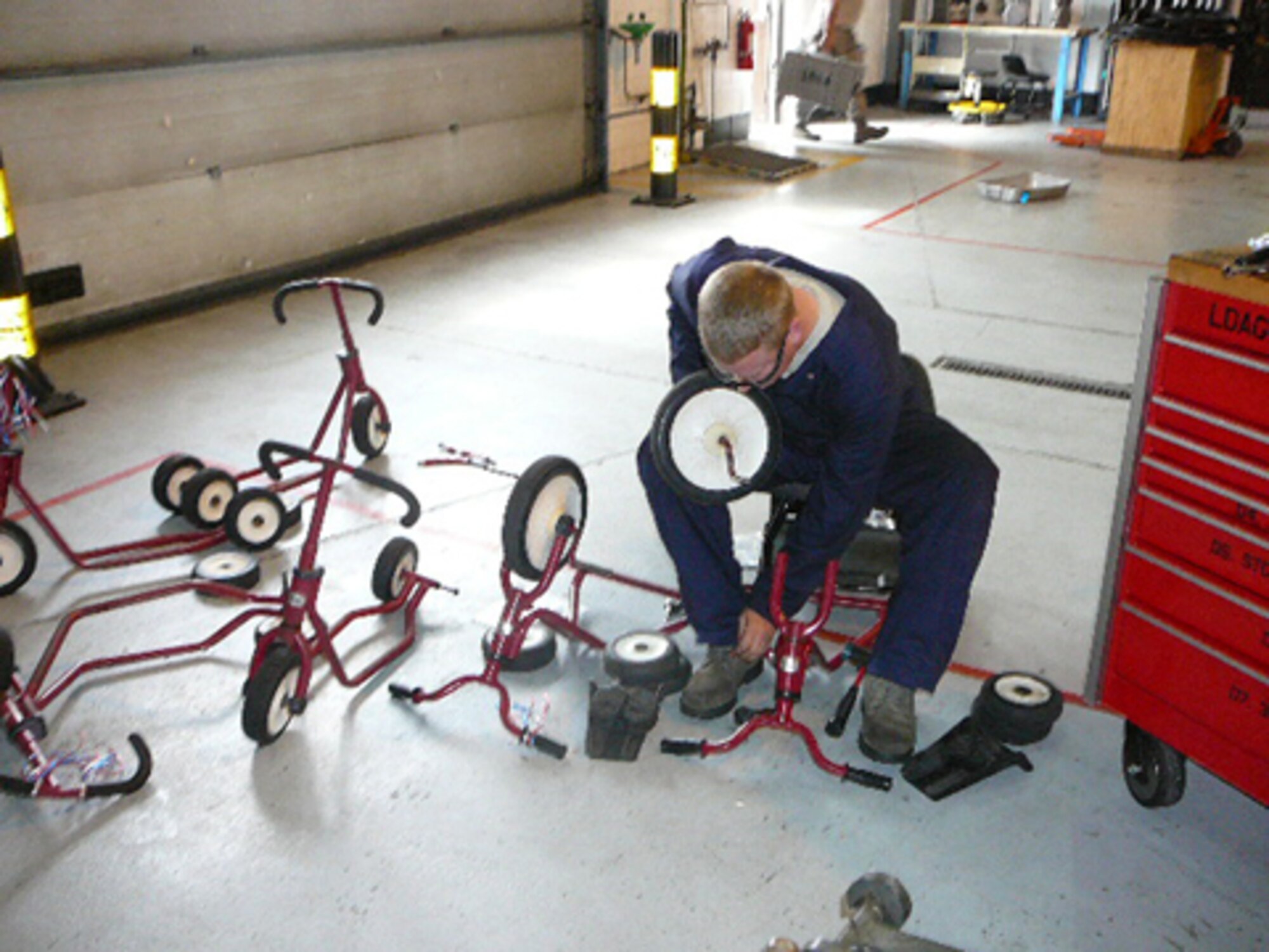 Staff Sgt. Jonathan Loeschke, The 48th Equipment Maintenance Squadron Aeorspace Ground Equipment flight Technician, removes the wheels on one of the Mildenhall CDC's tricycles before they get painted. The 48th EMS AGE flight volunteered to refurbish the tricycles, saving the CDC more than $3,500. (U.S. Air Force photo)