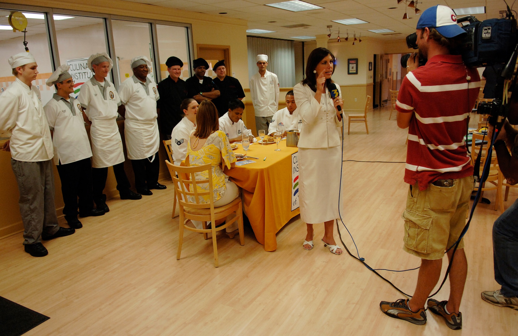 LANGLEY AIR FORCE BASE, Va. -- Stacy Davis, WTKR News Channel 3 reporter, broadcasts live from the Culinary Institute of Virginia in Norfolk, which is hosting an inter-service cook-off July 17. Three Langley airmen, Senior Airman Ashley Martinez, Senior Airman Kelmer Rapisora, and Airman 1st Class Ghil Medina, 1st Force Support Squadron food service journeymen, acted as judges. The cook-off was between two navy teams from the Norfolk Naval Air Station. (U.S. Air Force photo/Tech. Sgt. Levi Collins)